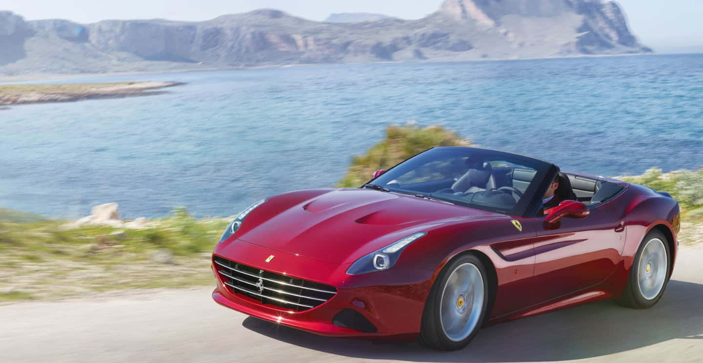 Ferrari California T 桌布 壁紙 — 一輛亮紅色法拉利 California 敞篷車沿著海岸公路疾駛，背景是碧綠的海水和岩石峭壁。