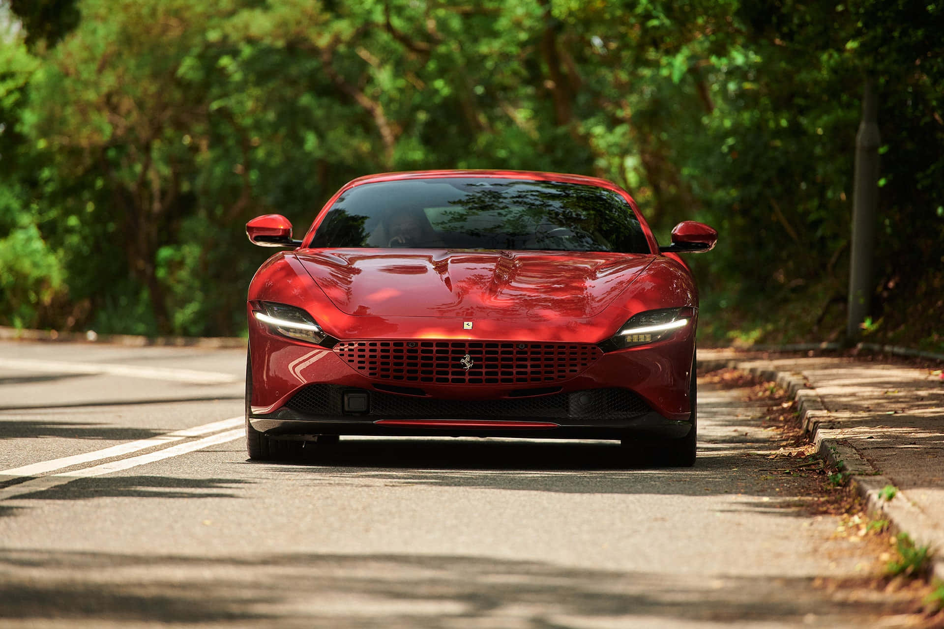 Ferrari Roma 桌布 壁紙 — 一輛光亮的紅色法拉利跑車在樹蔭斑駁的道路上向前行駛。