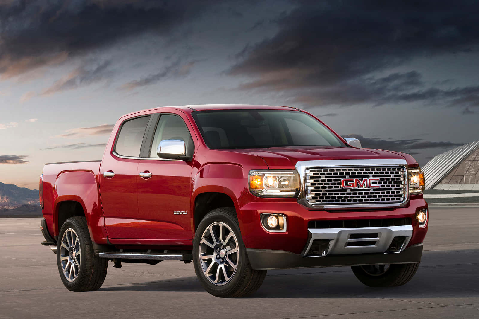 Gmc Canyon 桌布 壁紙 — 一輛光澤的紅色 GMC Canyon 皮卡車停在鋪砌路面上，背景是戲劇性的暮色天空和遠山。