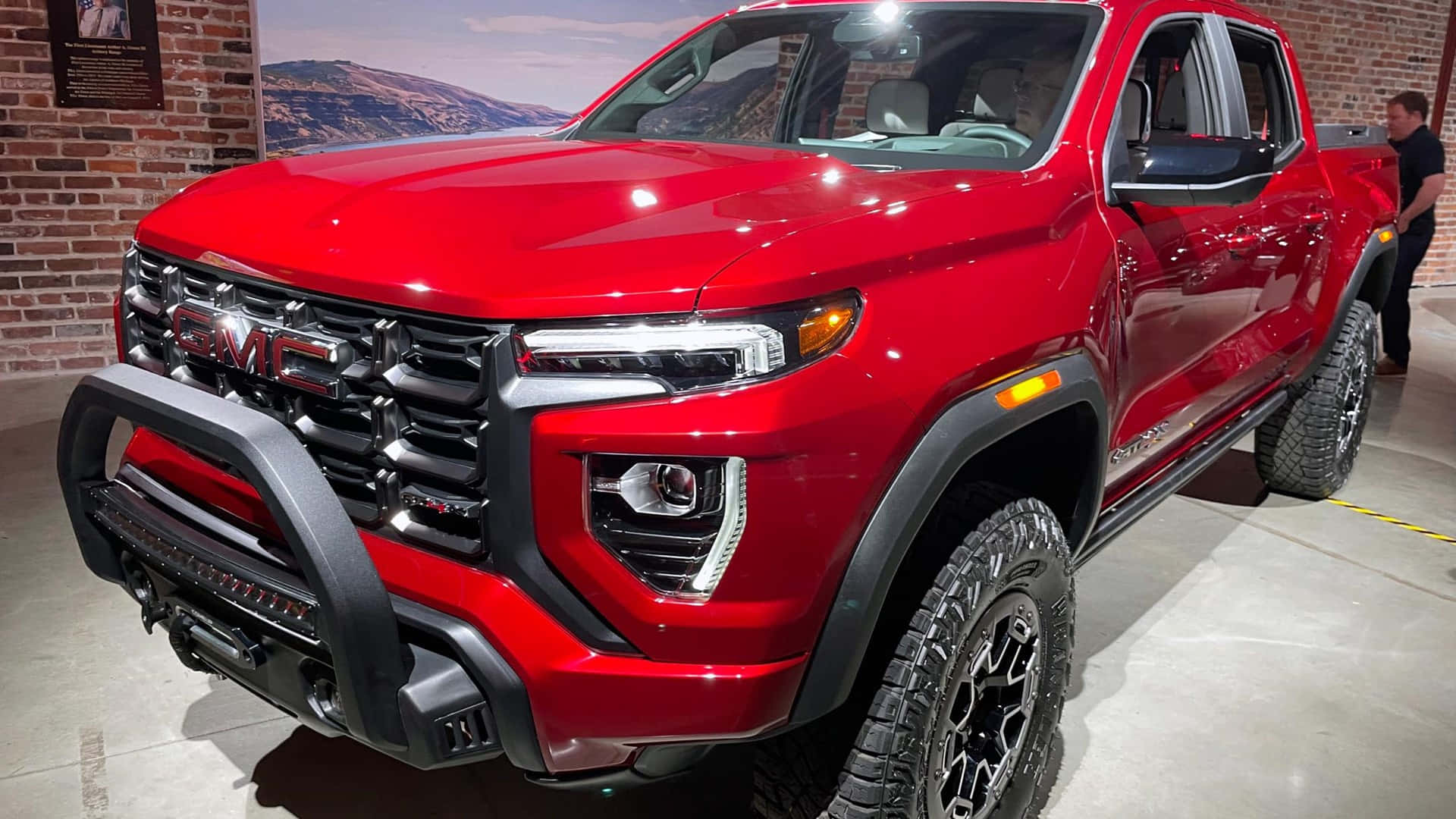 Gmc Canyon 桌布 壁紙 — 一輛光澤紅色GMC Sierra AT4皮卡車，帶有黑色飾邊和越野輪胎，在明亮的燈光下室內展示。