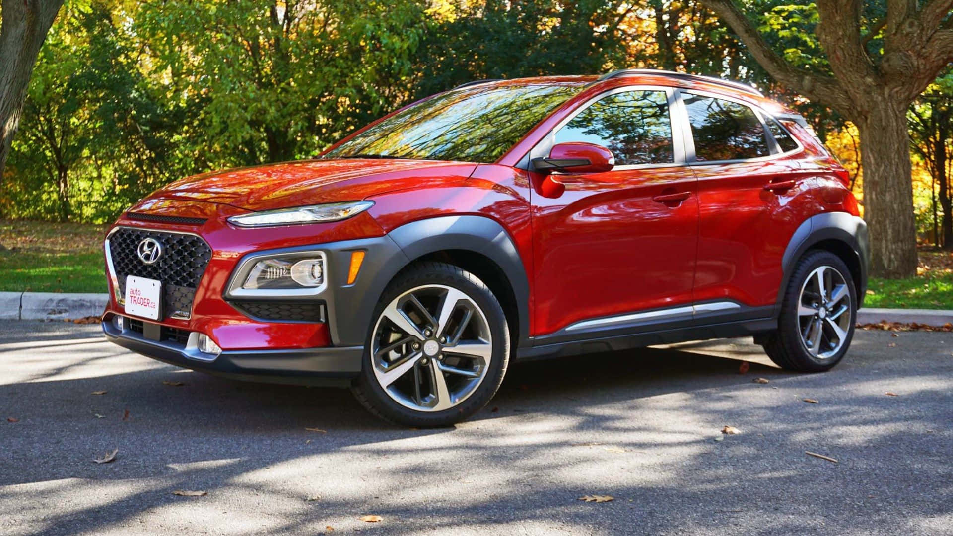 Hyundai Kona 桌布 壁紙 — 一輛亮紅色的現代Kona SUV停泊在樹蔭街道上，人行道散落著秋葉。