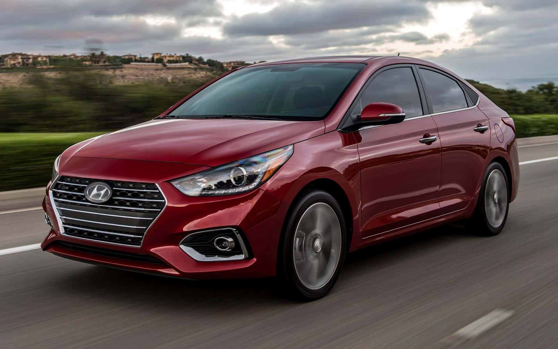 Hyundai Accent 桌布 壁紙 — 一輛亮紅色現代轎車在高速公路上疾駛，背景是模糊的綠樹和陰天。