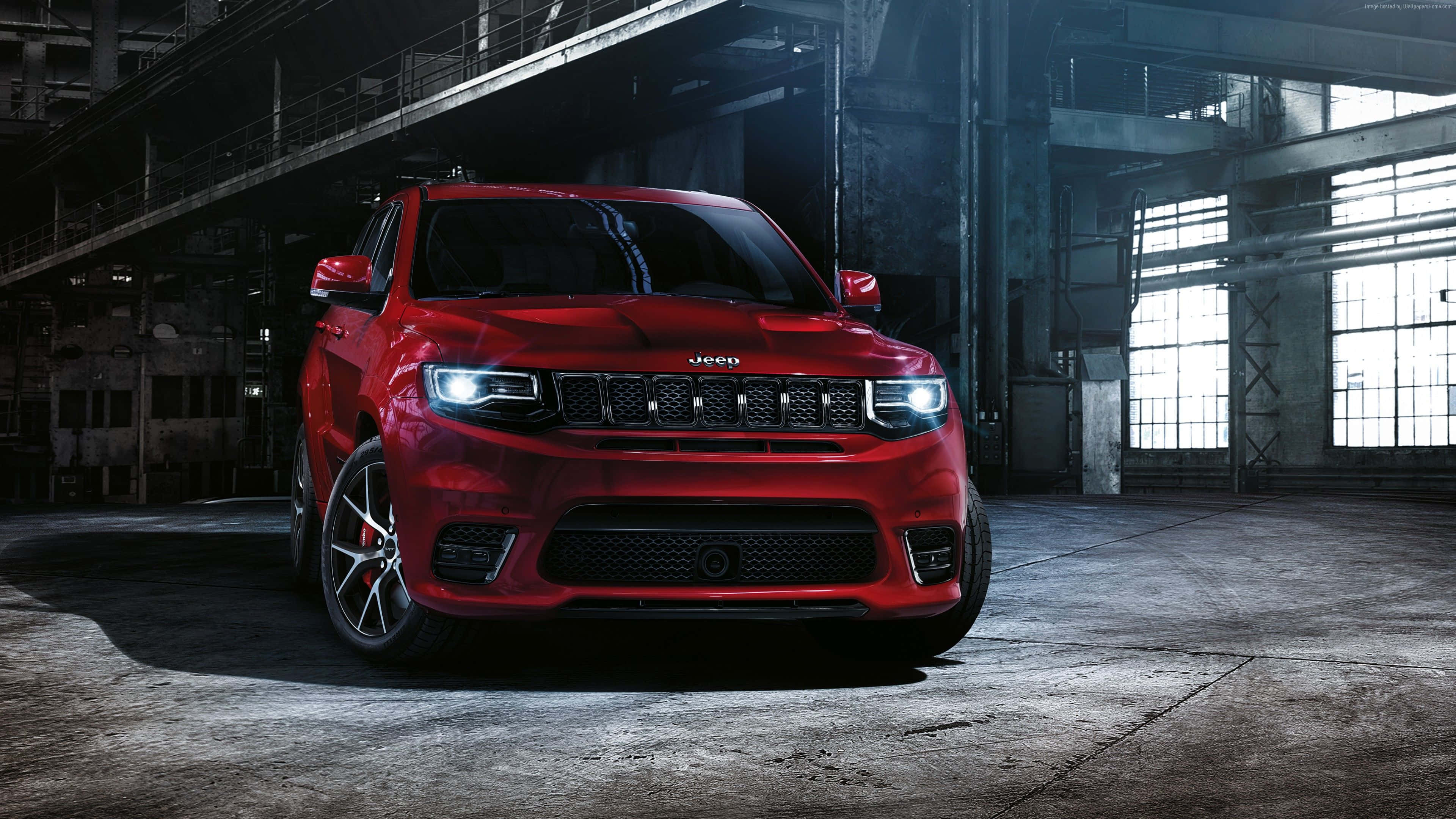 Jeep Grand Cherokee 桌布 壁紙 — 一輛亮面紅色Jeep Wrangler大膽地停放在一個昏暗的工業倉庫中，倉庫有高天花板和鋼樑。