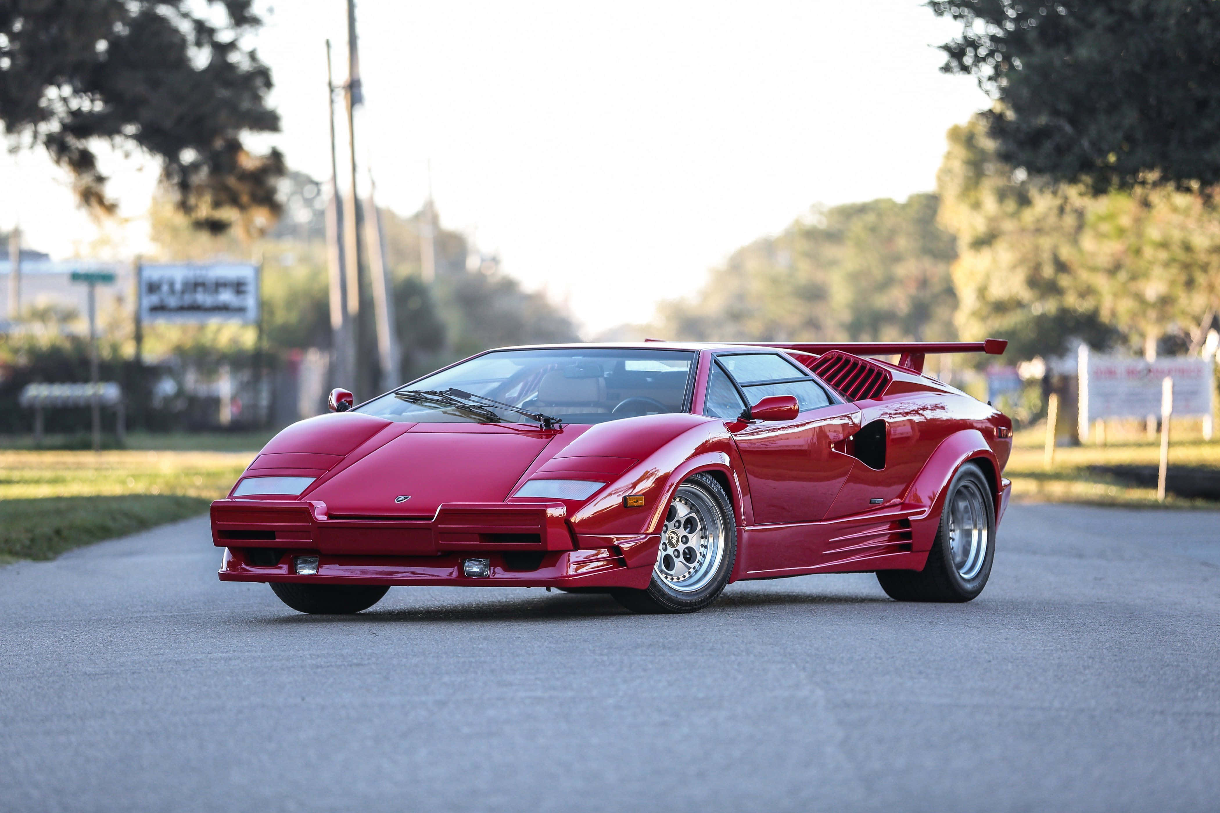 Lamborghini Countach 桌布 壁紙 — 一輛亮紅色藍寶堅尼Countach在金色夕陽光輝沐浴下的林蔭大道上飛馳。