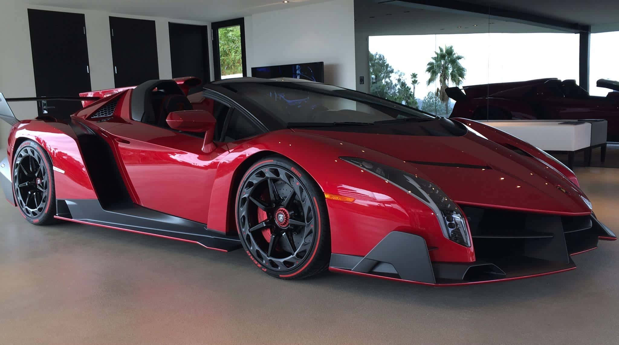 Lamborghini Veneno 桌布 壁紙 — 一輛光澤的紅色藍寶堅尼 Veneno 敞篷跑車在明亮的室內燈光下，在一個時尚的現代車庫中閃閃發光，外面可以看到棕櫚樹。