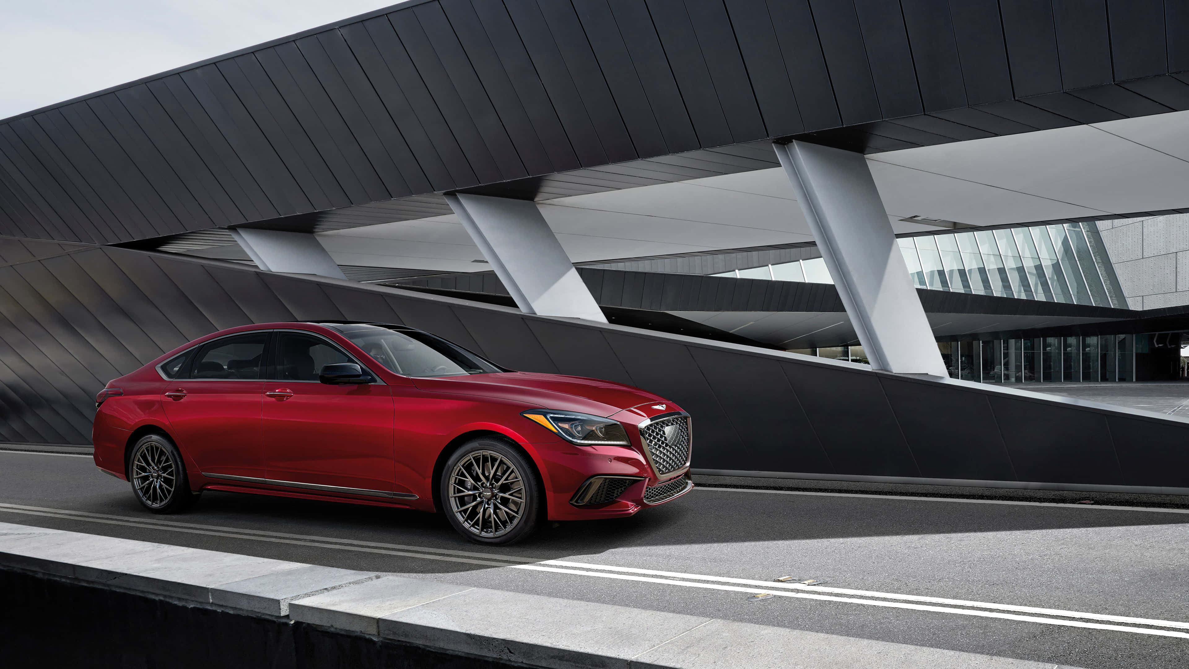Genesis G80 桌布 壁紙 — 一輛光澤的紅色豪華轎車在線條銳利的時尚現代建築高架橋下滑行。
