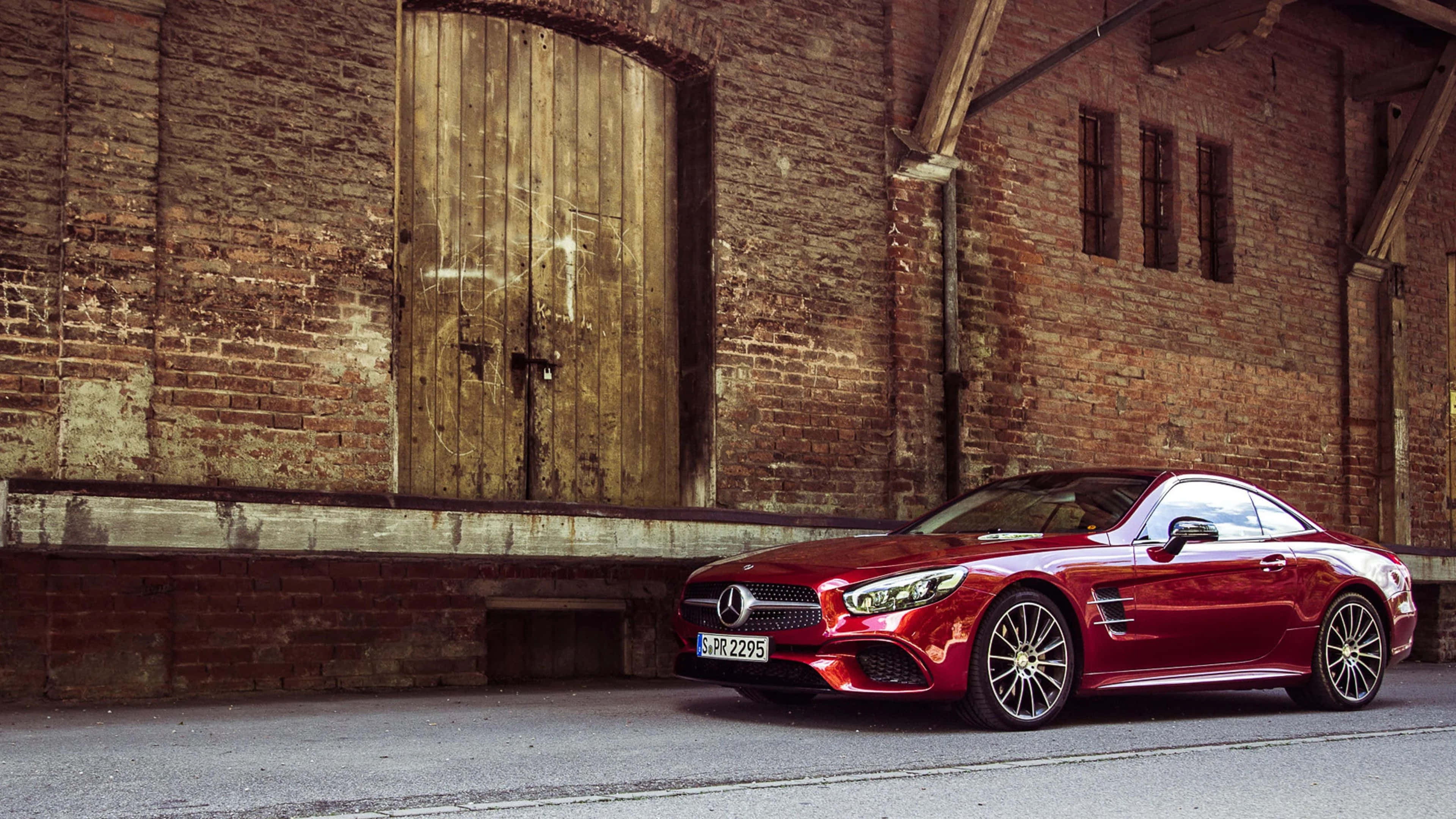 Mercedes Benz Sl-class 桌布 壁紙 — 一輛亮紅色賓士AMG SL63跑車停放在一個帶有大型木門、風化了的磚倉庫前。