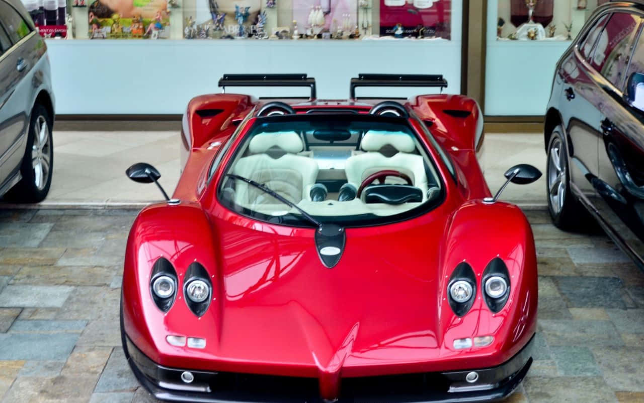 Pagani Zonda C12 Roadster 桌布 壁紙 — 一輛光澤紅色帕加尼Zonda跑車，配備白色內裝，在豪華展示間中與另外兩輛高端車輛一同展示。