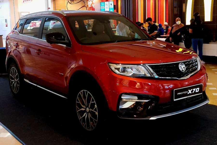 Proton X70 桌布 壁紙 — 一輛光澤的紅色Proton X70 SUV在室內展示，背景中有人在觀察。