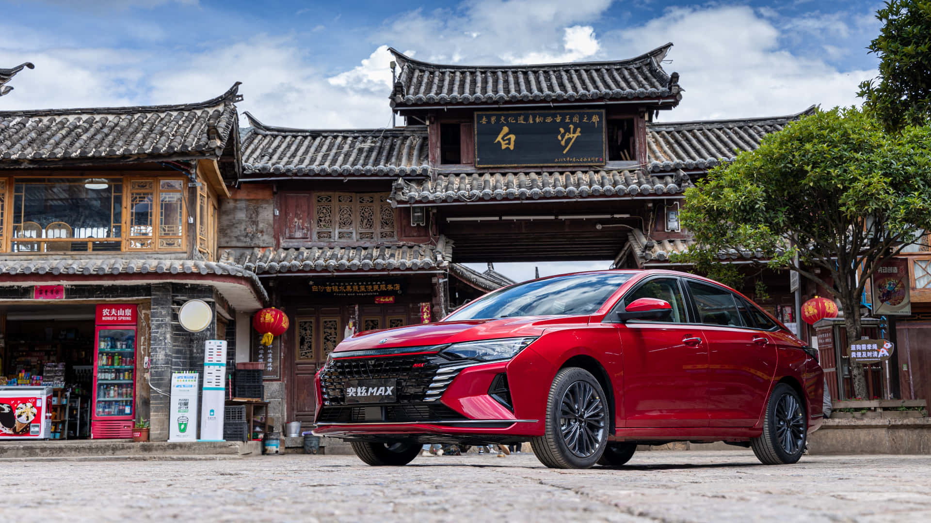 Dongfeng 桌布 壁紙 — 一輛光澤的紅色轎車停在鵝卵石路上，前方是傳統中式大門，有瓦片屋頂和懸掛的燈籠，天空部分多雲。