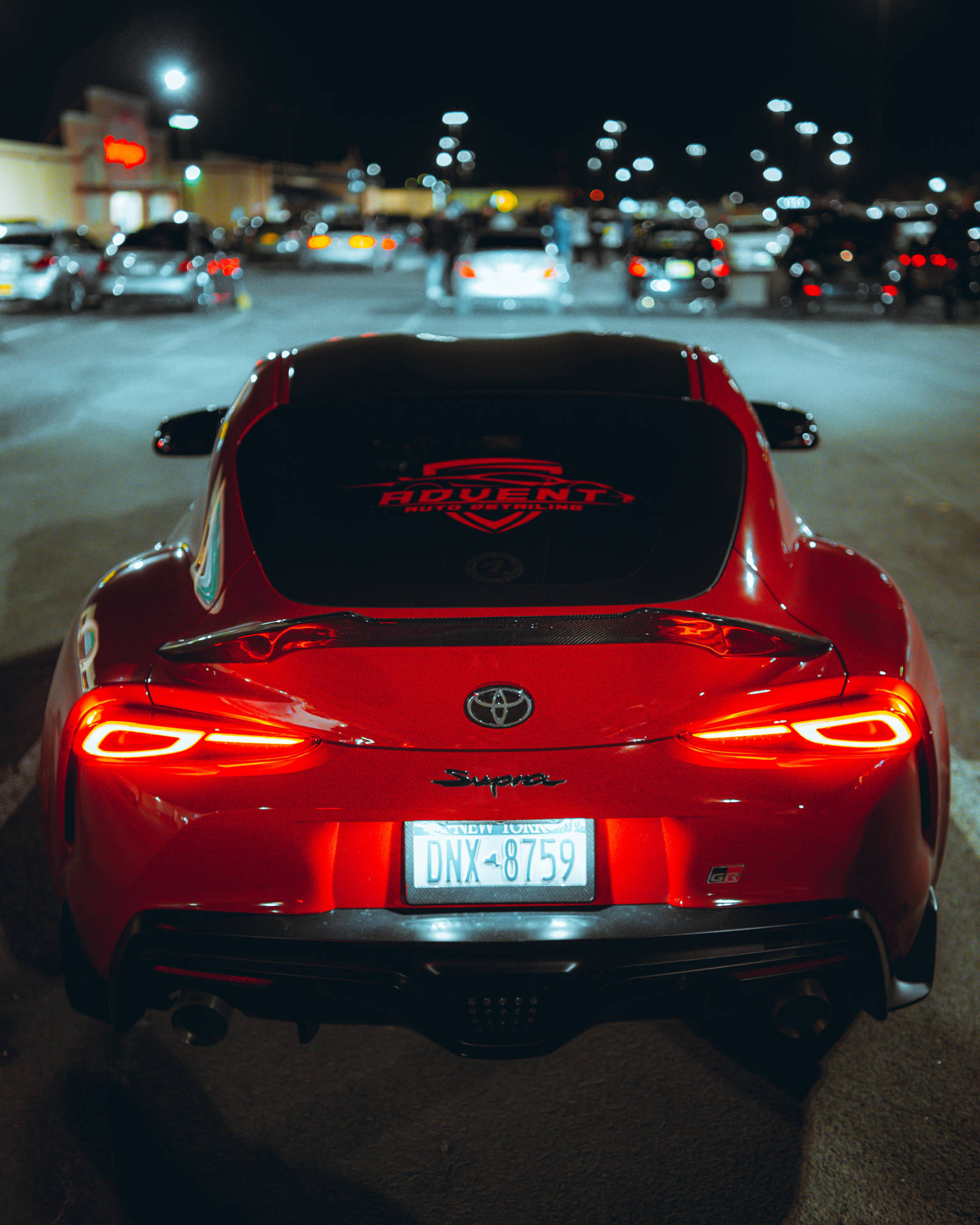 夜間城市停車場中停泊的紅色跑車，尾燈發光。 — Toyota Supra 壁紙
