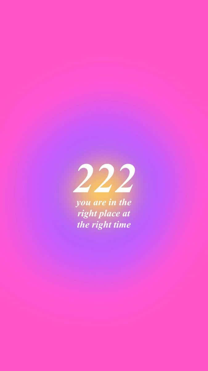  壁紙 — 粉紅色和紫色的發光漸變背景圍繞著數字222和短語你在正確的地方在正確的時間散發光芒。