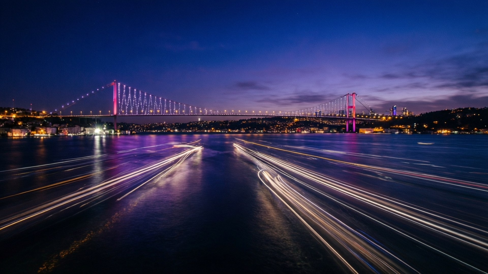 Bosphorus Bridge Light Trails 壁紙 — 長時間曝光捕捉到在暮色中，宏偉亮燈的吊橋下船隻發出的發光光跡。