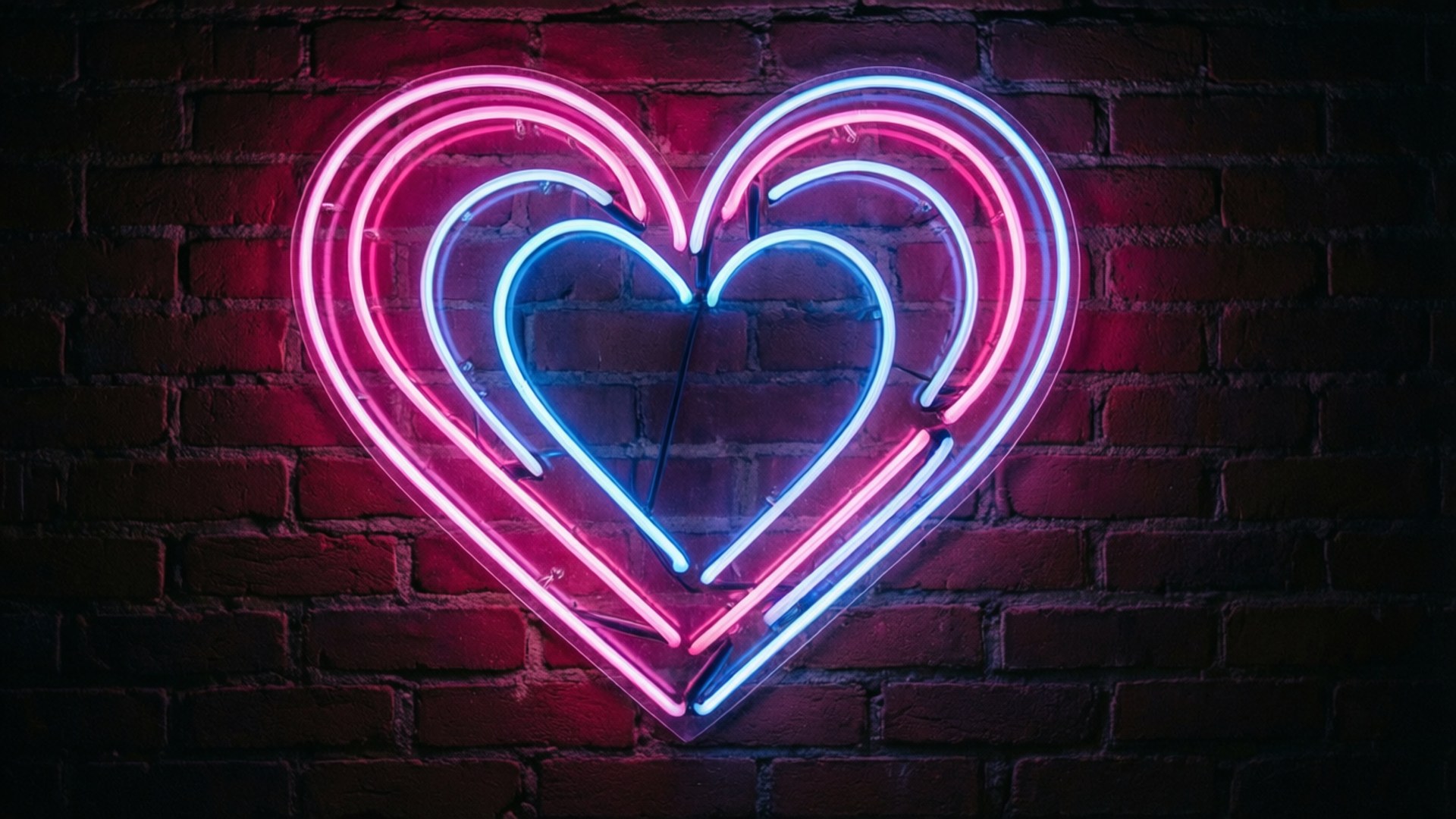 Neon Heart Glow 壁紙 — 一個發光的粉紅色和藍色霓虹心形標誌，以鮮豔的光跡照亮黑暗的磚牆。