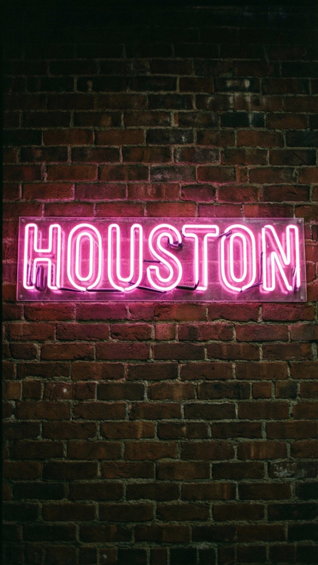 HOUSTON Neon Sign 壁紙 — 一個發光的粉紅色霓虹燈牌，拼出 houston，在深色紋理磚牆上投射出鮮豔的色彩。