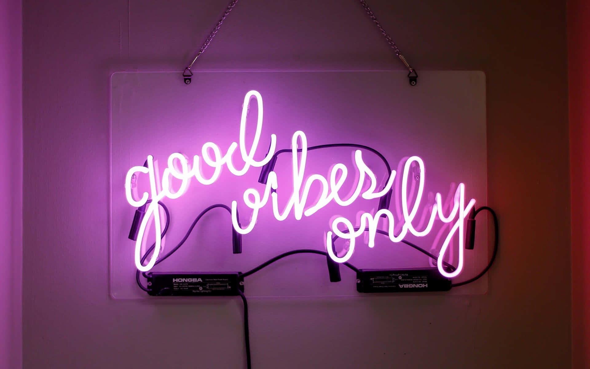  壁紙 — 一個發光的粉紅色霓虹燈牌，上面寫著「good vibes only」，掛在牆上，投射出柔和的紫色光線。