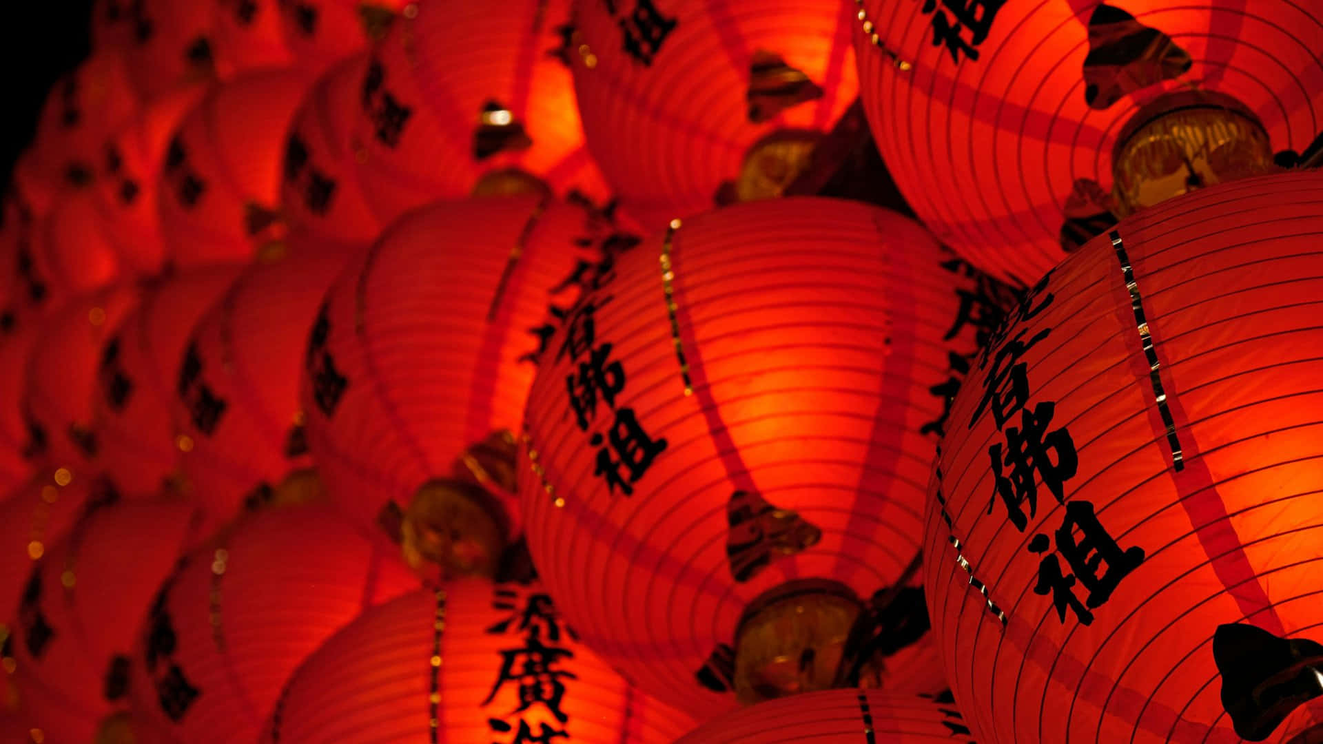  壁紙 — 一簇密集的紅色紙燈籠，上面有黑色中文字，照亮了節日的夜景。