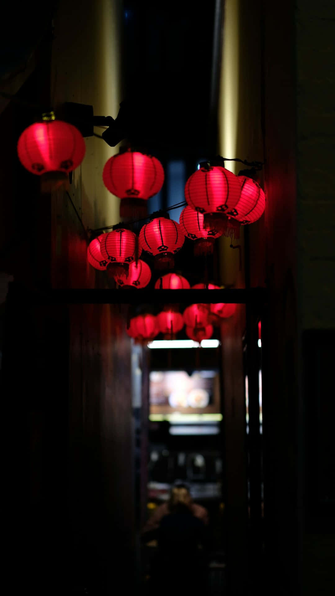  壁紙 — 發光的紅色紙燈籠懸掛在光線昏暗的小巷中，將溫暖的光線投射在深色木樑上。