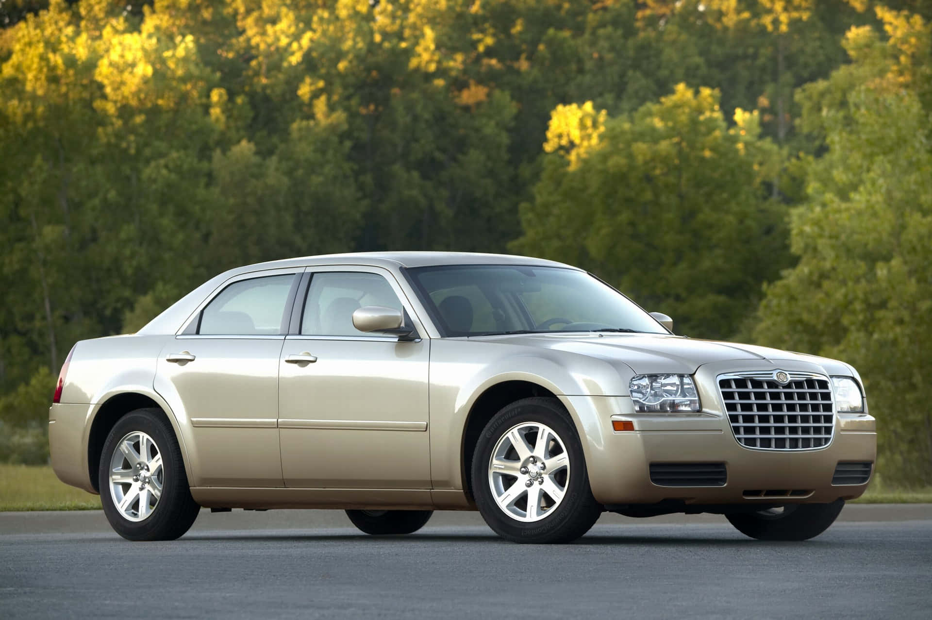 Chrysler 300 桌布 壁紙 — 一輛金色克萊斯勒300轎車停在瀝青路上，背景中秋天的樹木閃耀著光芒。