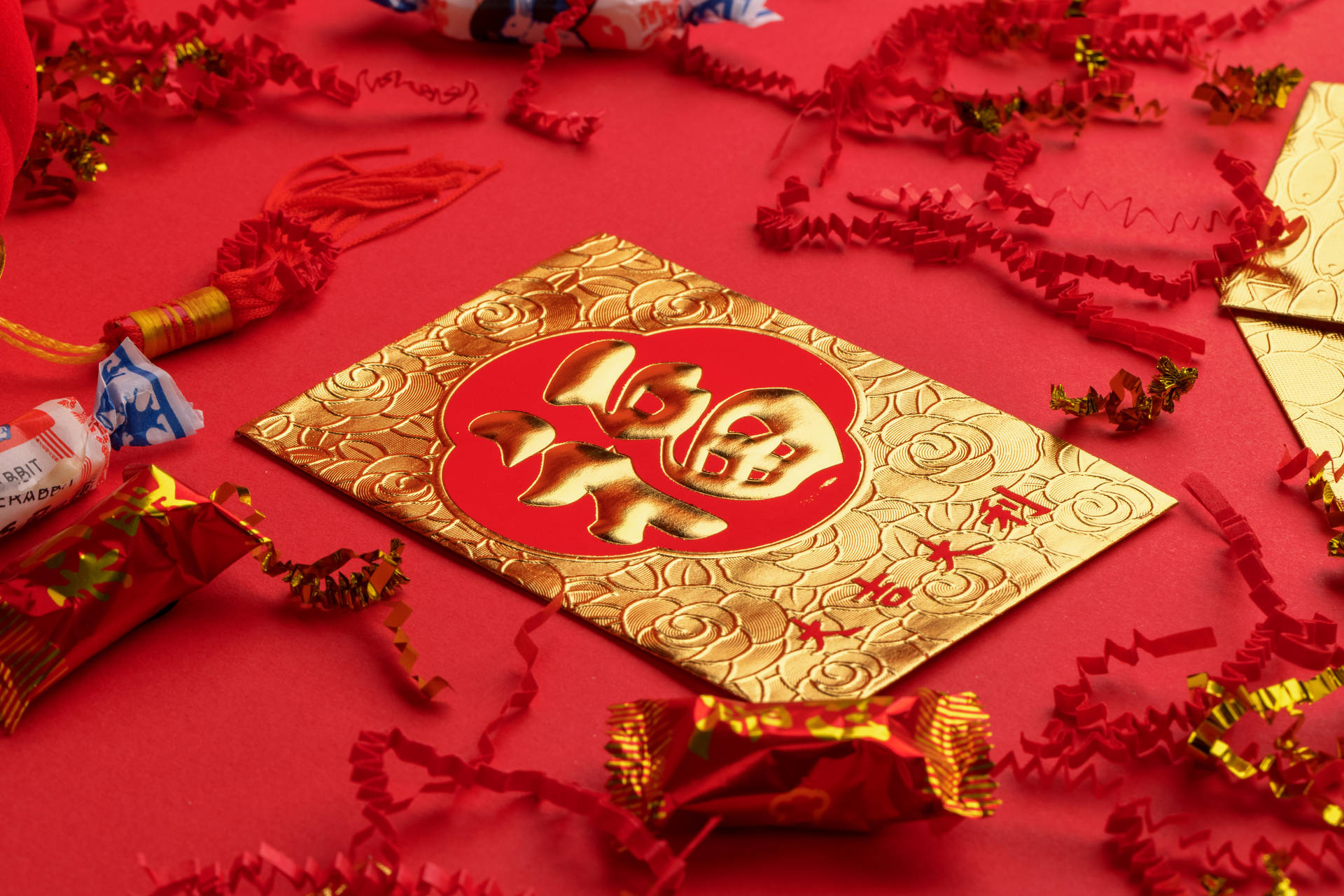 帶有金色中文字的紅包，周圍是喜慶的紙屑和糖果。 — 春節 壁紙