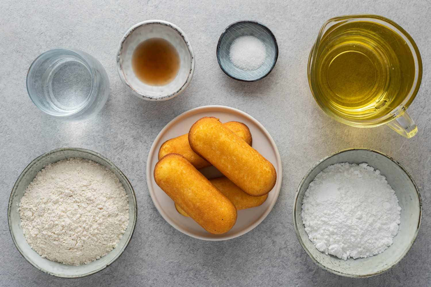  壁紙 — 金黃色的玉米熱狗放在盤子上，周圍有碗裝的麵粉、糖、水和油，置於灰色檯面上。