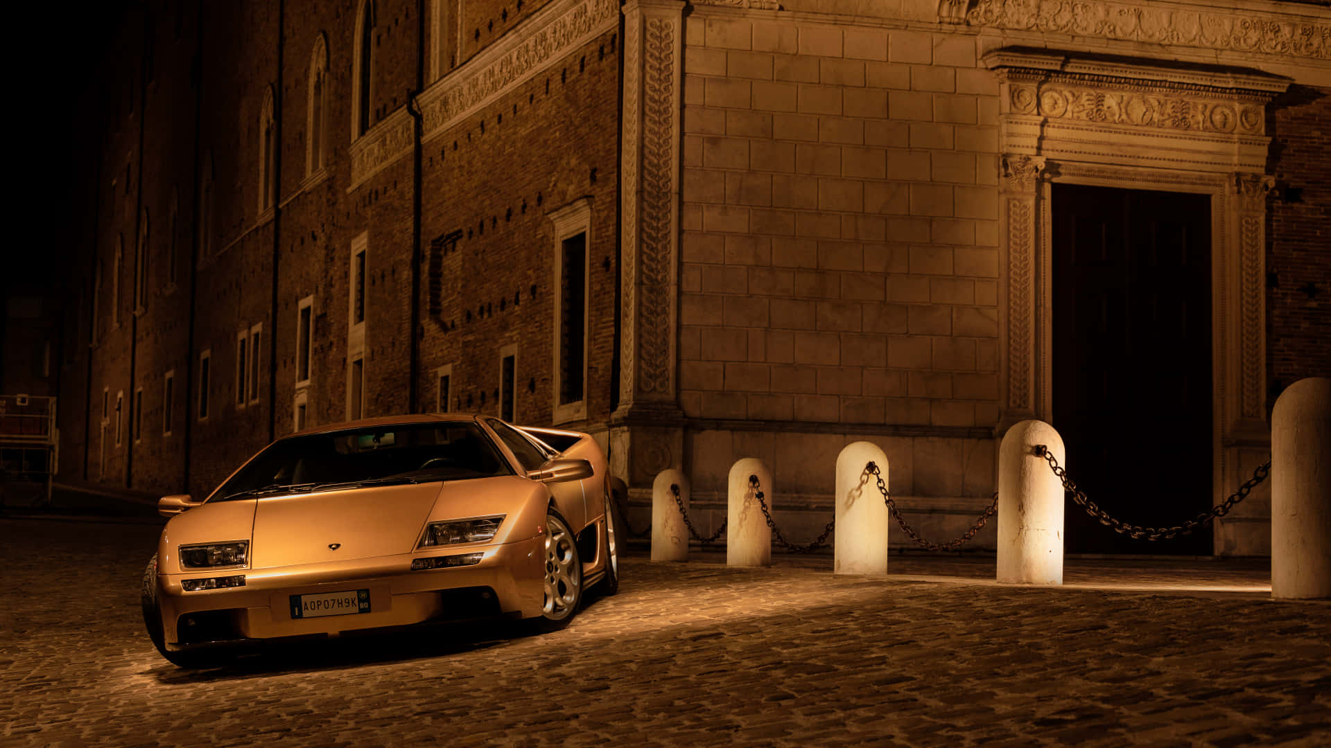 Lamborghini Diablo 桌布 壁紙 — 一輛金色藍寶堅尼Diablo在夜晚停泊在鵝卵石街道上，旁邊是一座華麗的石建築。