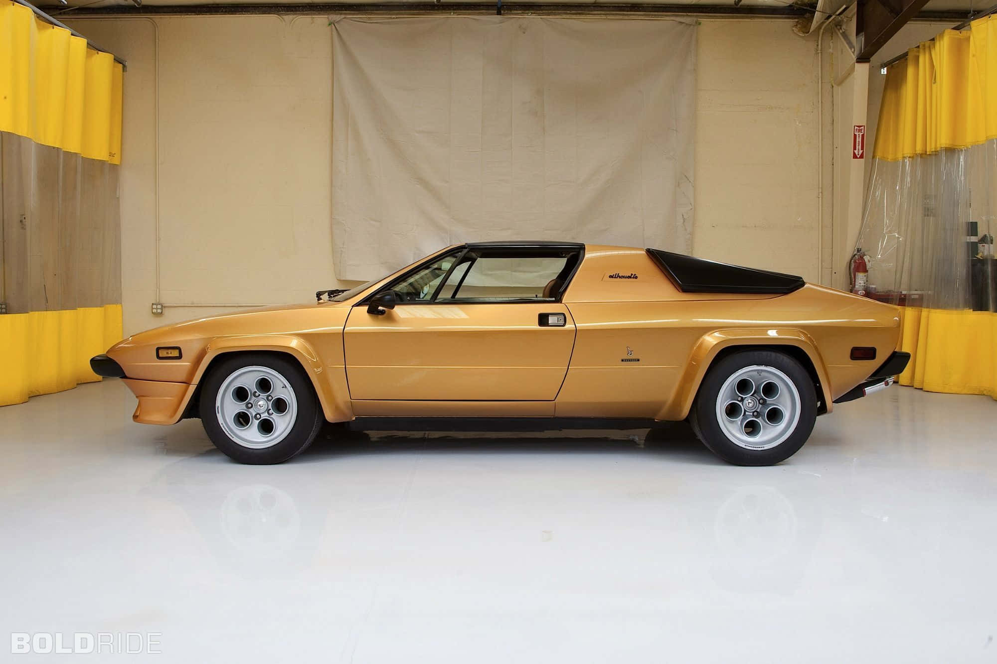 Lamborghini Silhouette 桌布 壁紙 — 一輛金色復古跑車帶有黑色點綴，展示在一個帶有黃色窗簾的潔白車庫中。