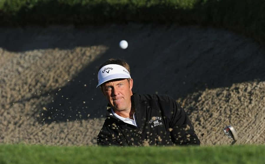高爾夫 桌布 壁紙 — Golfer mid-swing hitting ball out of sand bunker with sand spraying around him on sunny day.