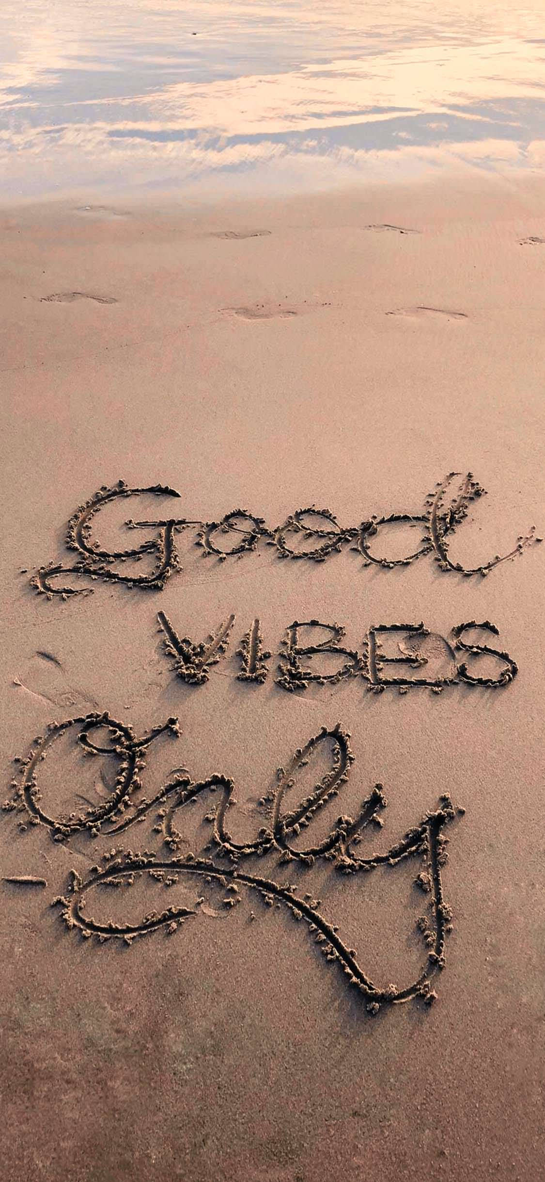 氛圍 桌布 壁紙 — 「Good Vibes Only」這句話以草書寫在濕沙上，背景有柔和的海浪和天空倒影。