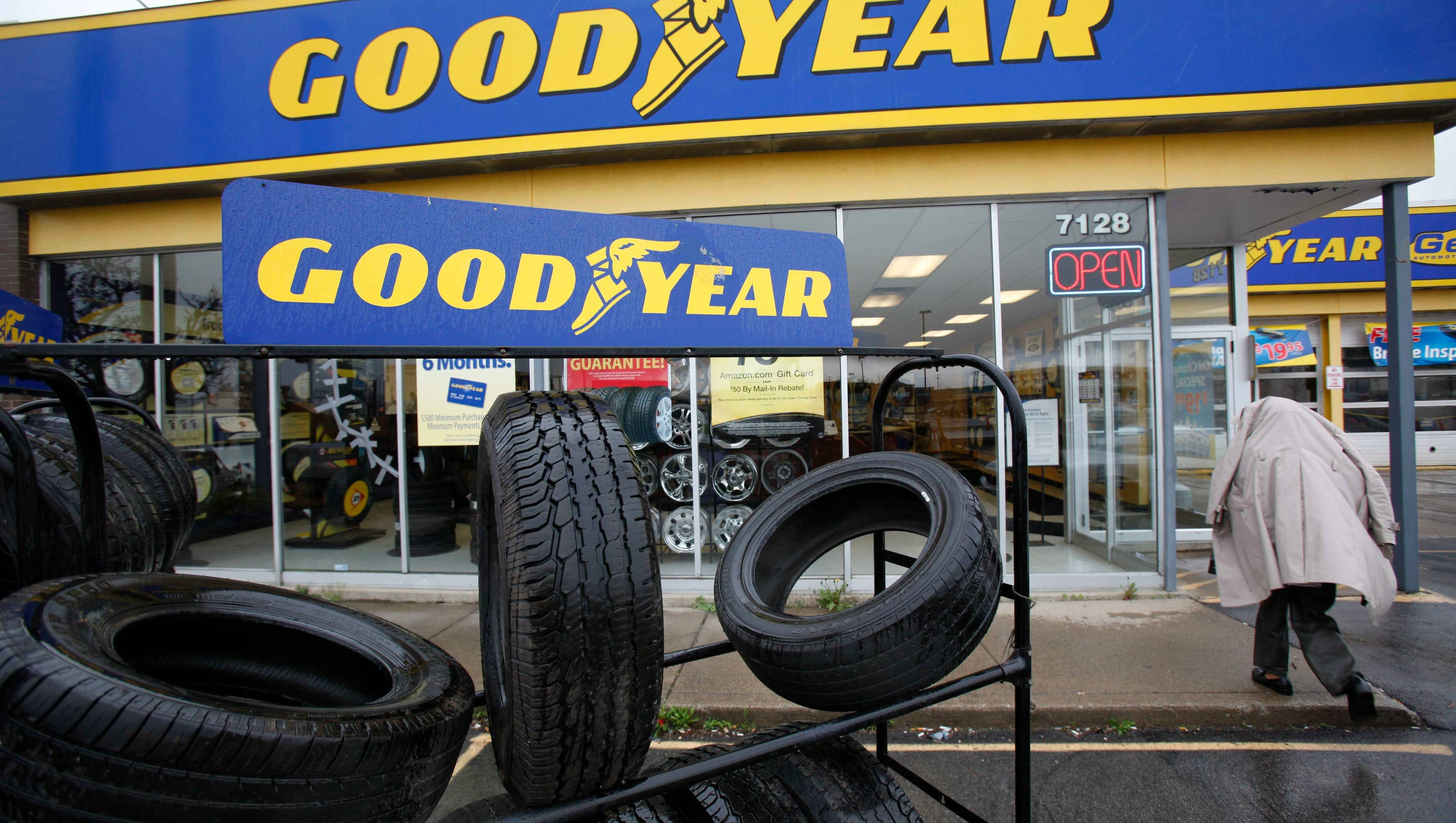 cars 桌布 壁紙 — Goodyear輪胎店外觀，堆疊的輪胎和一個穿外套的人走在濕漉漉的人行道上。