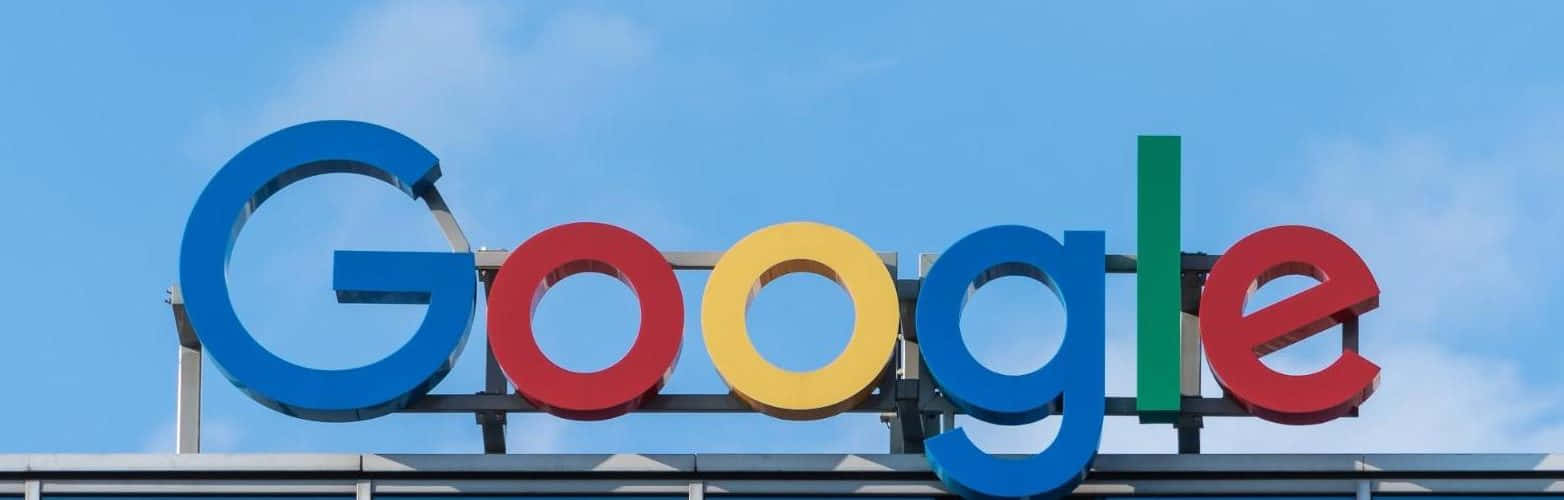 google 桌布 壁紙 — Google 標誌性的多色標誌在晴朗藍天和薄雲襯托下顯得格外醒目。