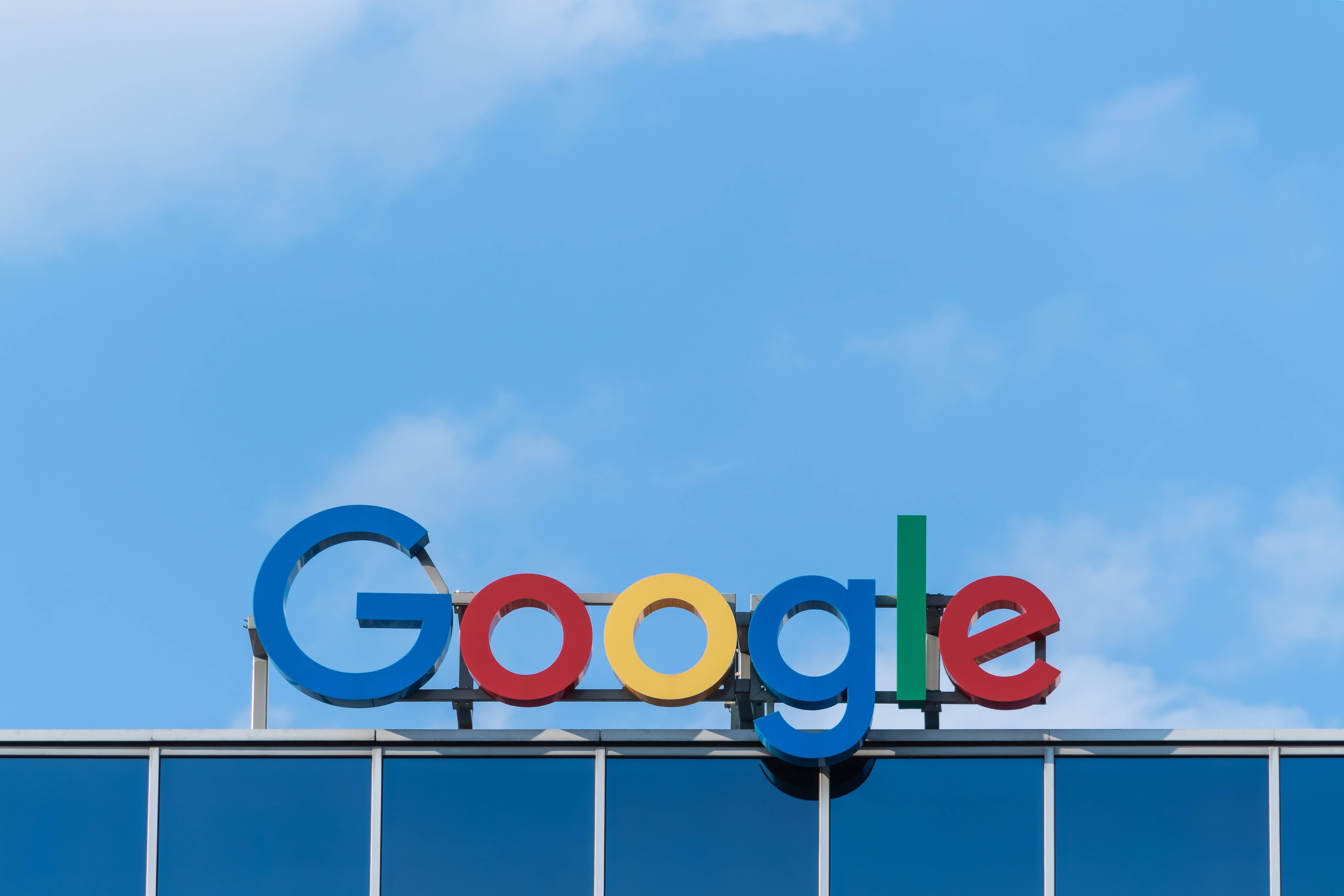 google 桌布 壁紙 — Google 色彩繽紛的標誌在現代玻璃建築上方的清澈藍天下顯得格外醒目。