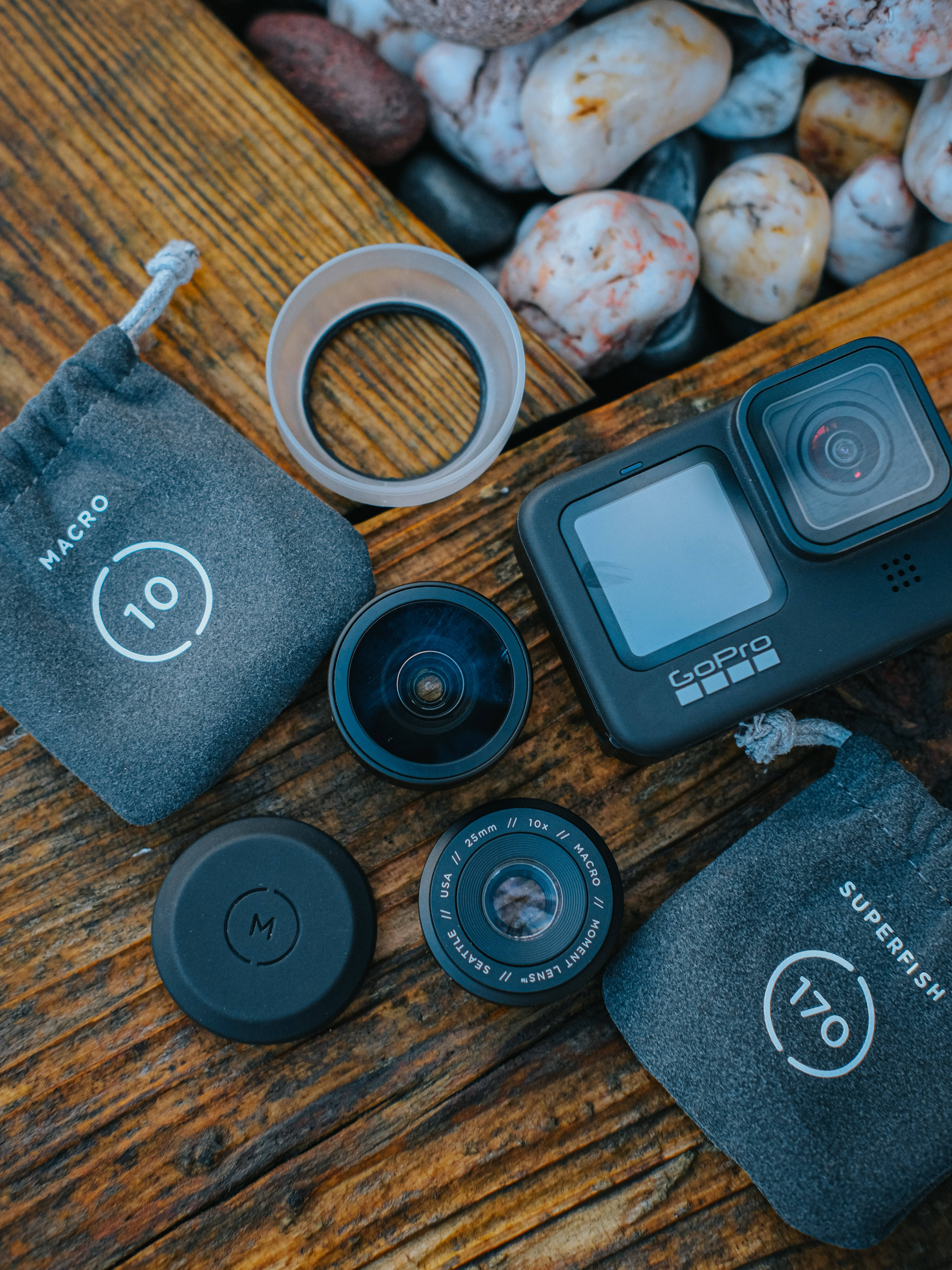 攝影 桌布 壁紙 — GoPro相機及其微距超級魚眼鏡頭排列在質樸的木質表面上，旁邊是光滑的河石。