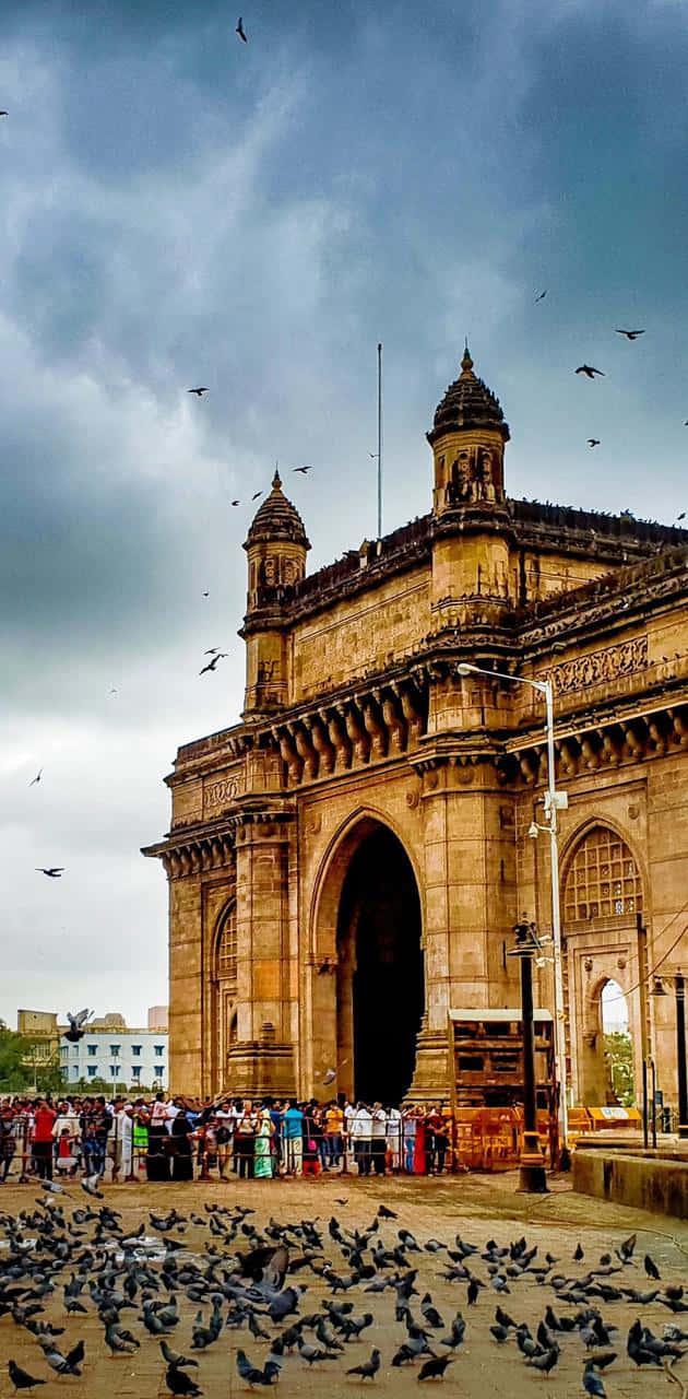印度 桌布 壁紙 — Grand Gateway of India monument under cloudy sky with crowds and pigeons flocking around its base.