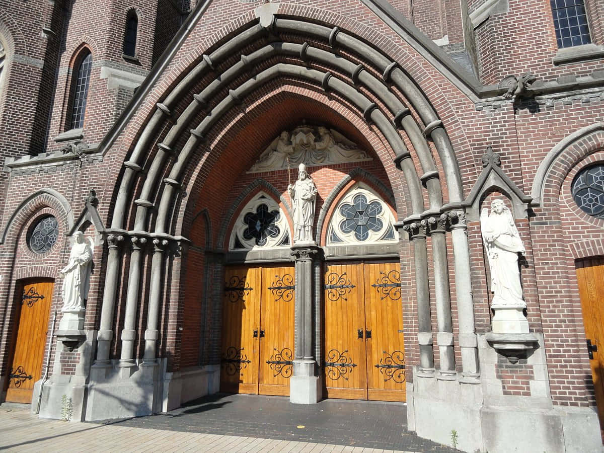 Tilburg 桌布 壁紙 — 宏偉的哥德式教堂入口，擁有紅磚拱門、華麗木門和白色雕像，在明亮的日光下。