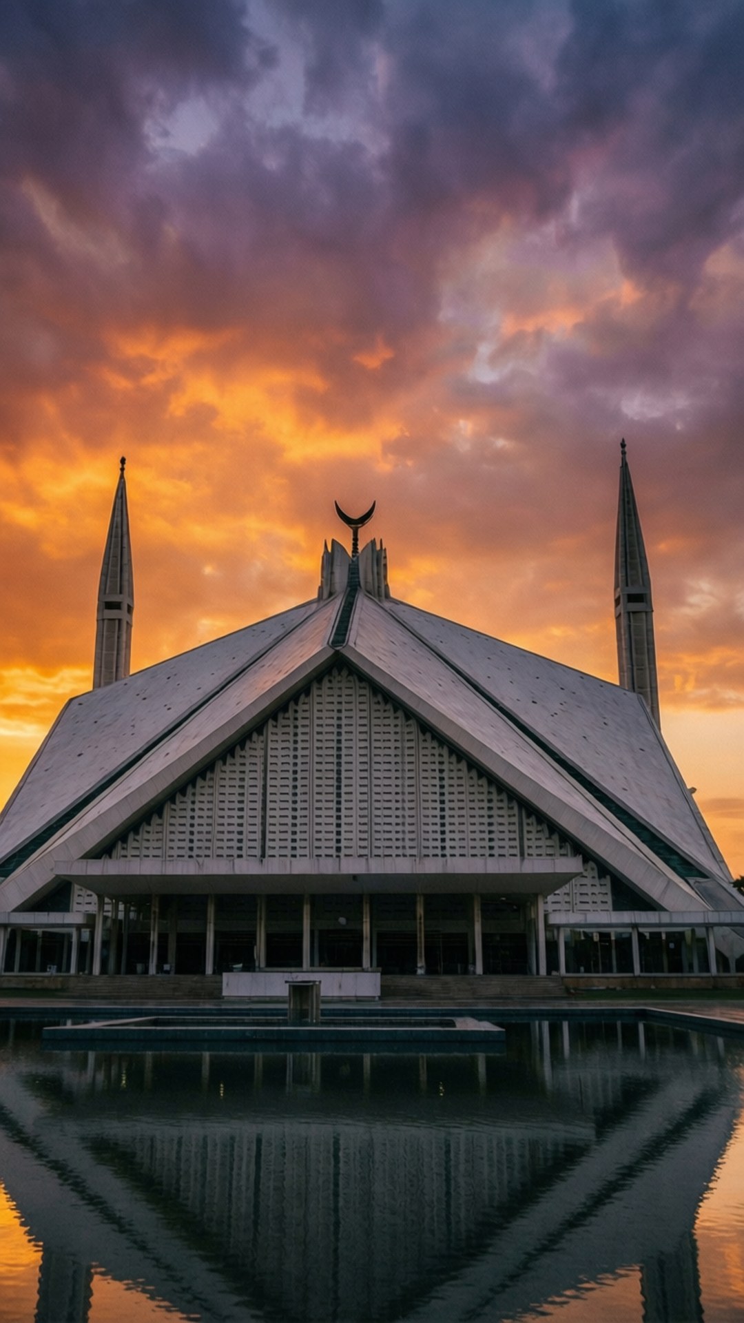 Faisal Mosque Sunset 壁紙 — 一座宏偉的現代清真寺，擁有尖尖的宣禮塔和新月標誌，在火紅的橙色和紫色日落天空的襯托下呈現剪影，其倒影完美地映照在平靜的前景水池中。