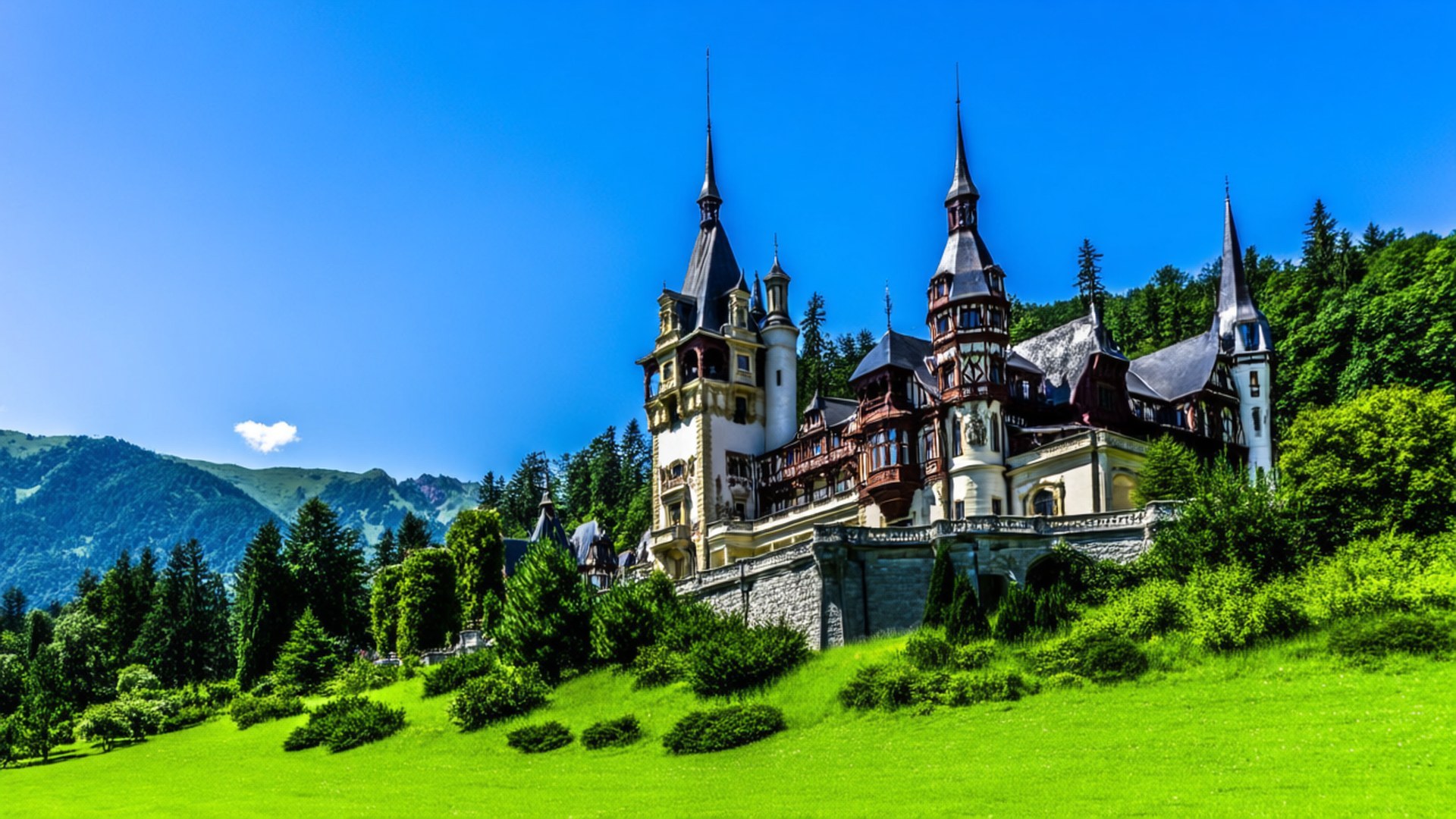 Peles Castle Fairytale 壁紙 — 一座宏偉華麗的城堡，擁有尖塔和角樓，坐落在鬱鬱蔥蔥的綠色山坡上，周圍環繞著茂密的森林和遠處的山脈，在清澈的藍天下。