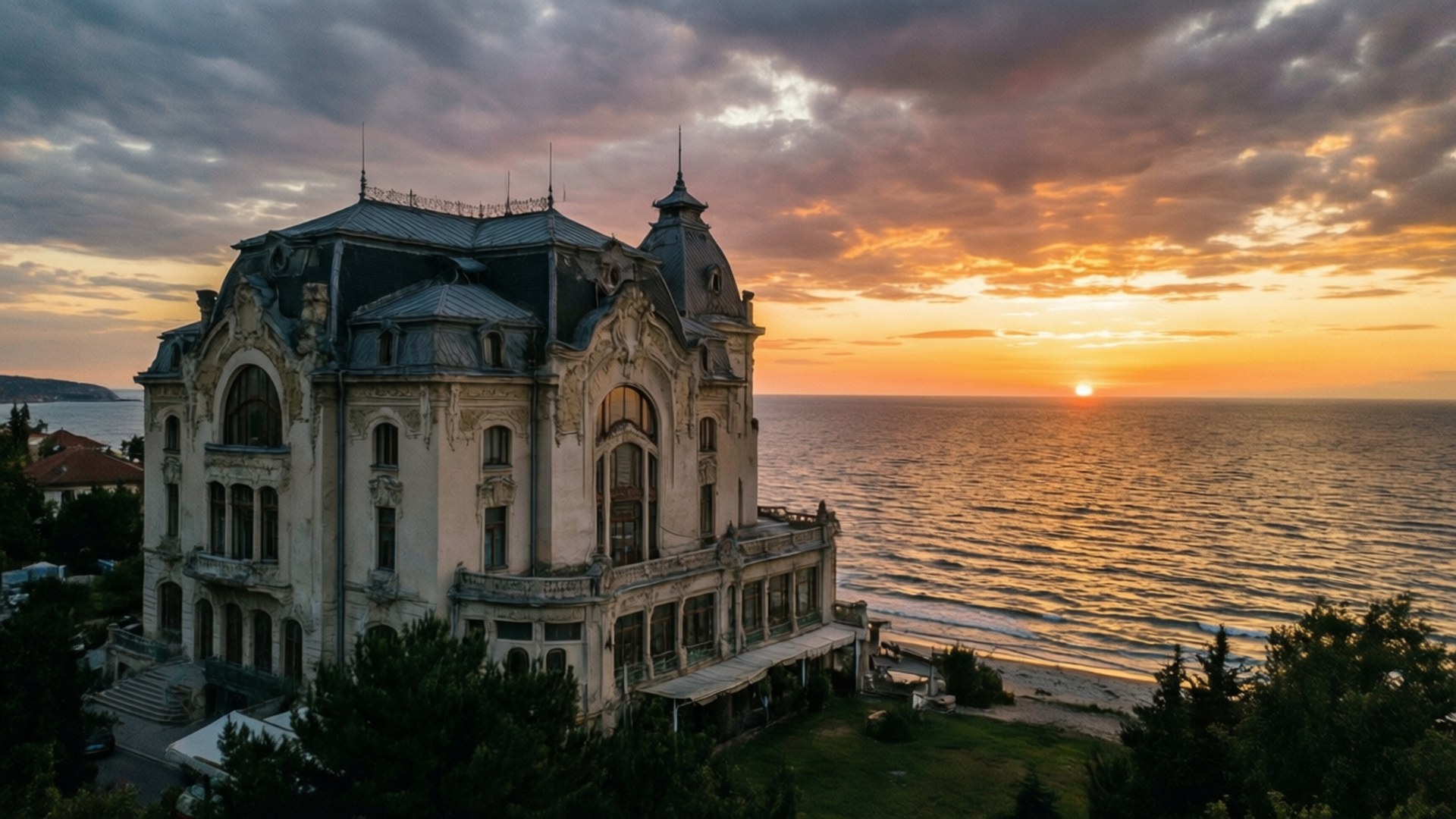 Constanta Casino Sunset 壁紙 — 一座宏偉華麗的大宅，深色屋頂和白色外牆，矗立在海邊，夕陽西下，金色天空，平靜水面。