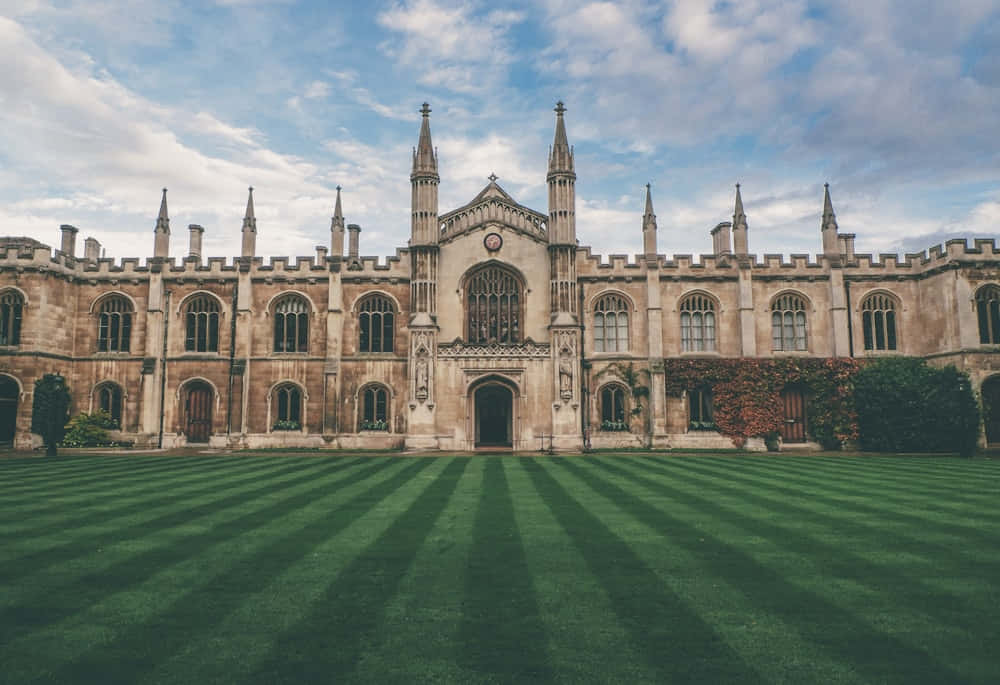 Oxford United Kingdom 桌布 壁紙 — 宏偉的石造大學建築，擁有尖頂和拱形窗戶，矗立在完美條紋的綠色草坪後面，天空部分多雲。