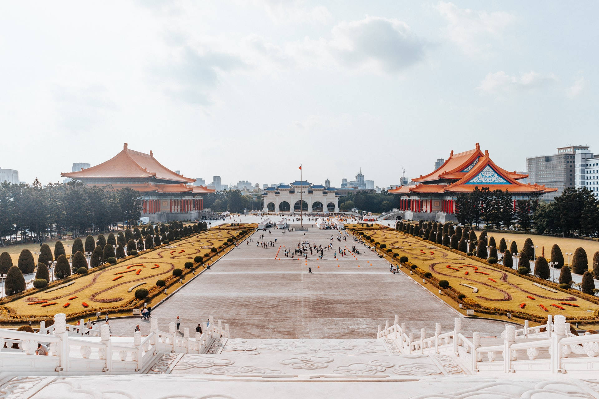 宏偉的宮殿建築群，擁有橙色屋頂和金色花園，上方是明亮的天空。 — 台北 壁紙