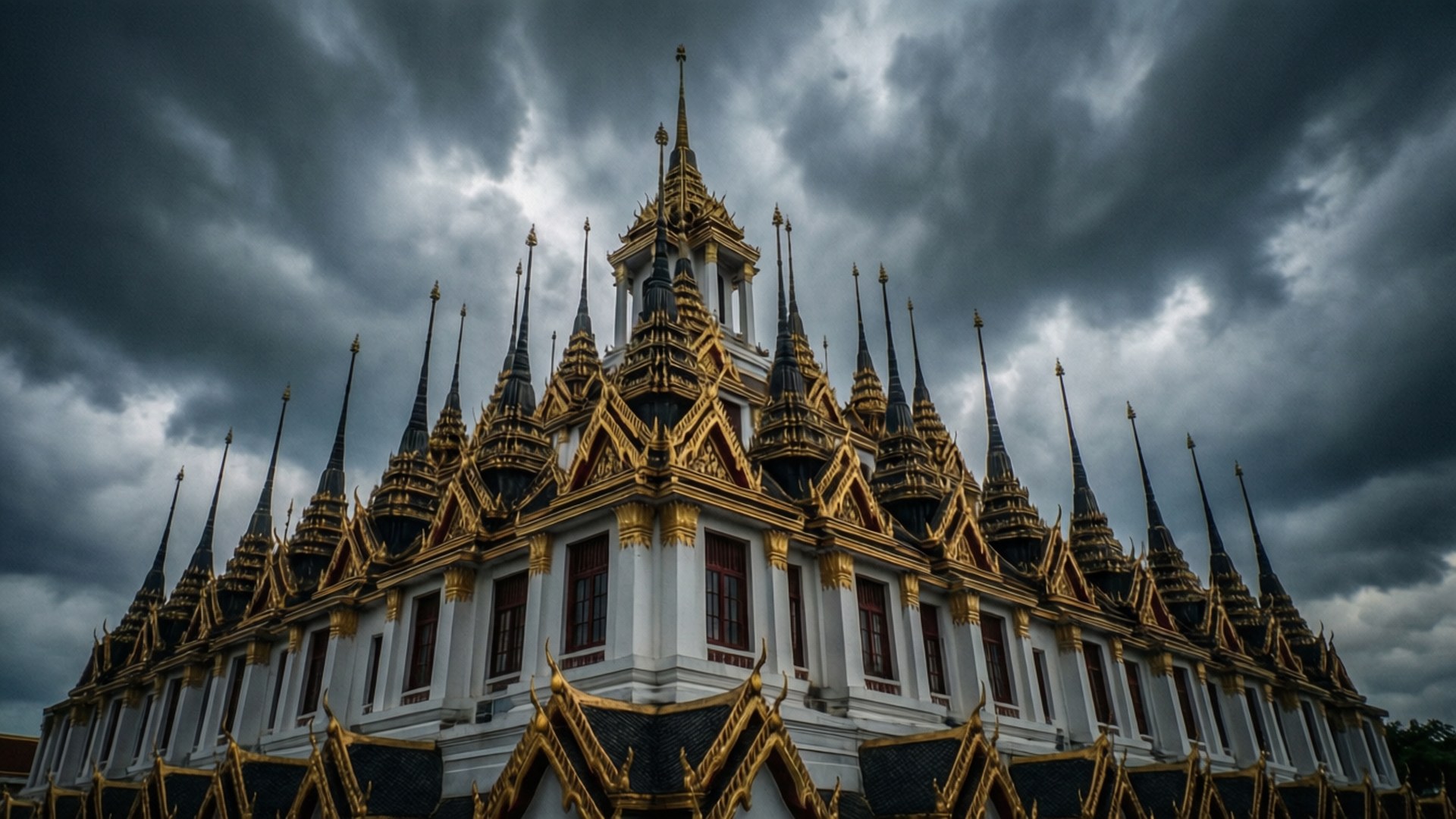 Loha Prasat Stormy Sky 壁紙 — 一座宏偉的泰國寺廟，金色尖頂和白色牆壁，矗立在戲劇性的暴風雨天空下。
