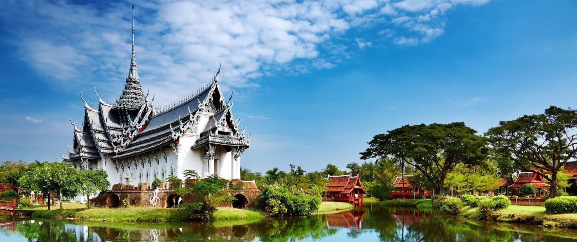 白色泰國寺廟倒映在平靜的水面上，周圍綠樹成蔭，藍天白雲。 — 廟宇 壁紙