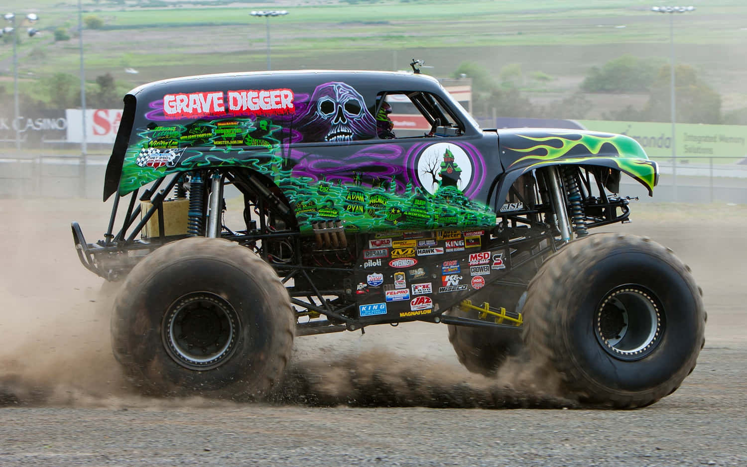 Truck 桌布 壁紙 — Grave Digger 怪獸卡車在泥地賽道上咆哮，噴出綠色、紫色和黑色的火焰，揚起塵土。