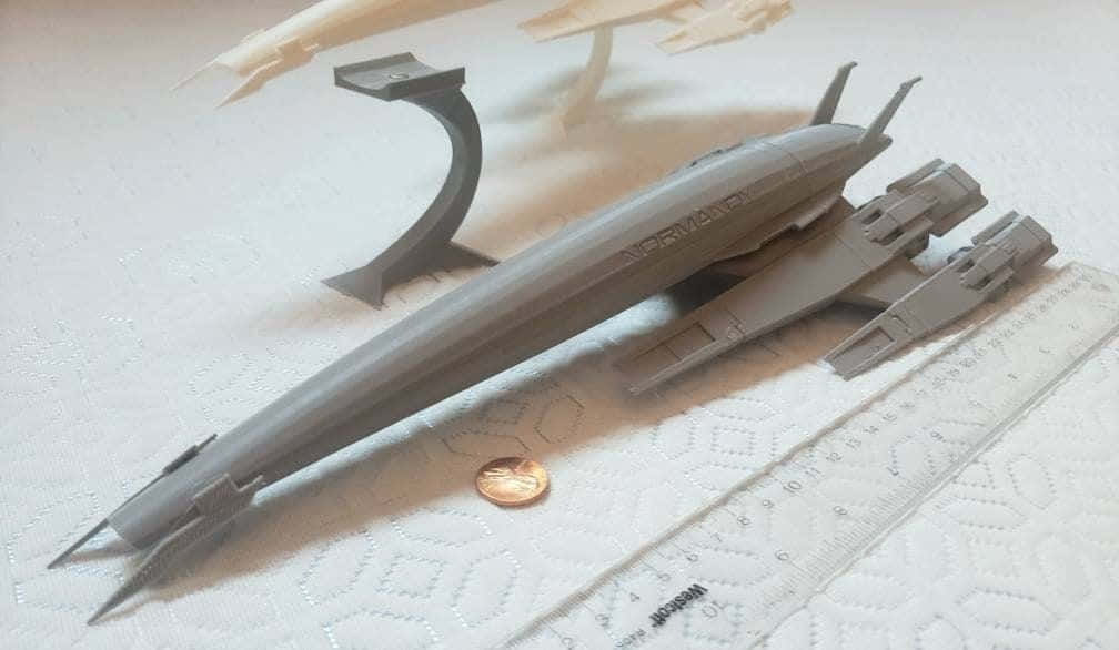 Normandy Sr-2 桌布 壁紙 — 一個灰色3D列印的太空船模型，標有「NORMA」，放置在帶有紋理的白色表面上，旁邊有尺子和硬幣作為比例參考。