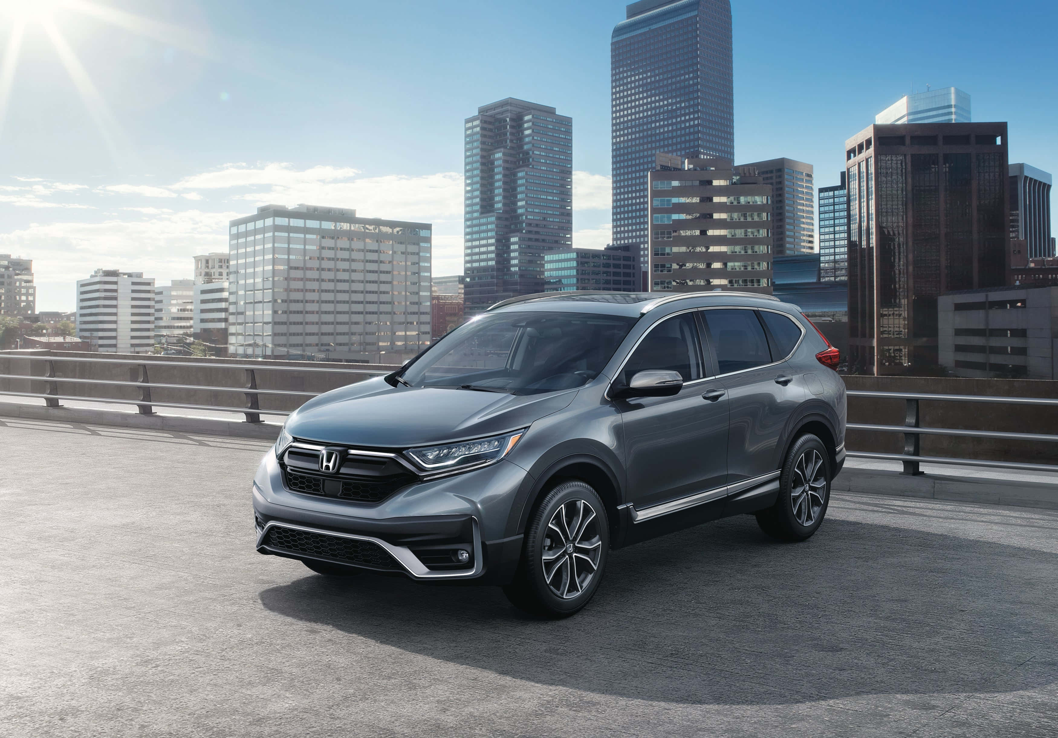 Honda Cr-v 桌布 壁紙 — 一輛流線型灰色本田CRV在陽光明媚的橋上行駛，背景是現代城市天際線。