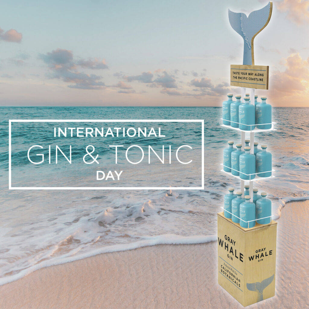 Gin 桌布 壁紙 — Gray Whale Gin 品牌的藍色琴酒瓶分層展示在沙灘上，伴隨著日落、海浪和鯨魚尾巴標誌。