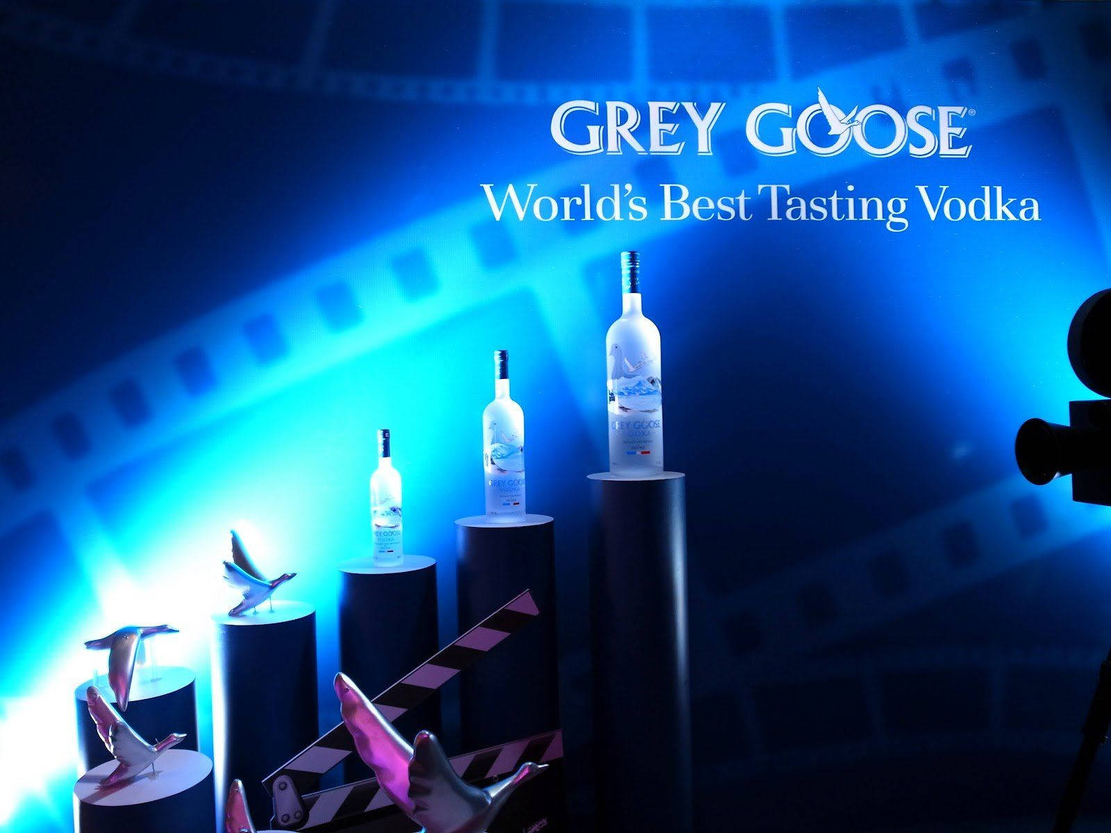 品牌 桌布 壁紙 — Grey Goose 伏特加酒瓶在藍色電影燈光下展示於底座上，背景為膠片條和場記板。