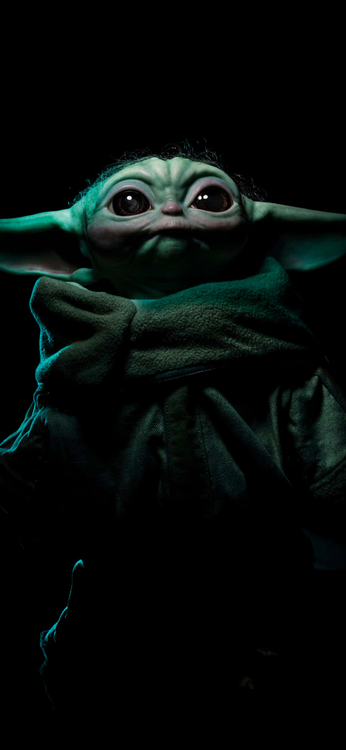 Baby Yoda iPhone 桌布 壁紙 — Grogu 的特寫，在黑色背景前發出青綠色光芒，包裹在有質感的長袍中。