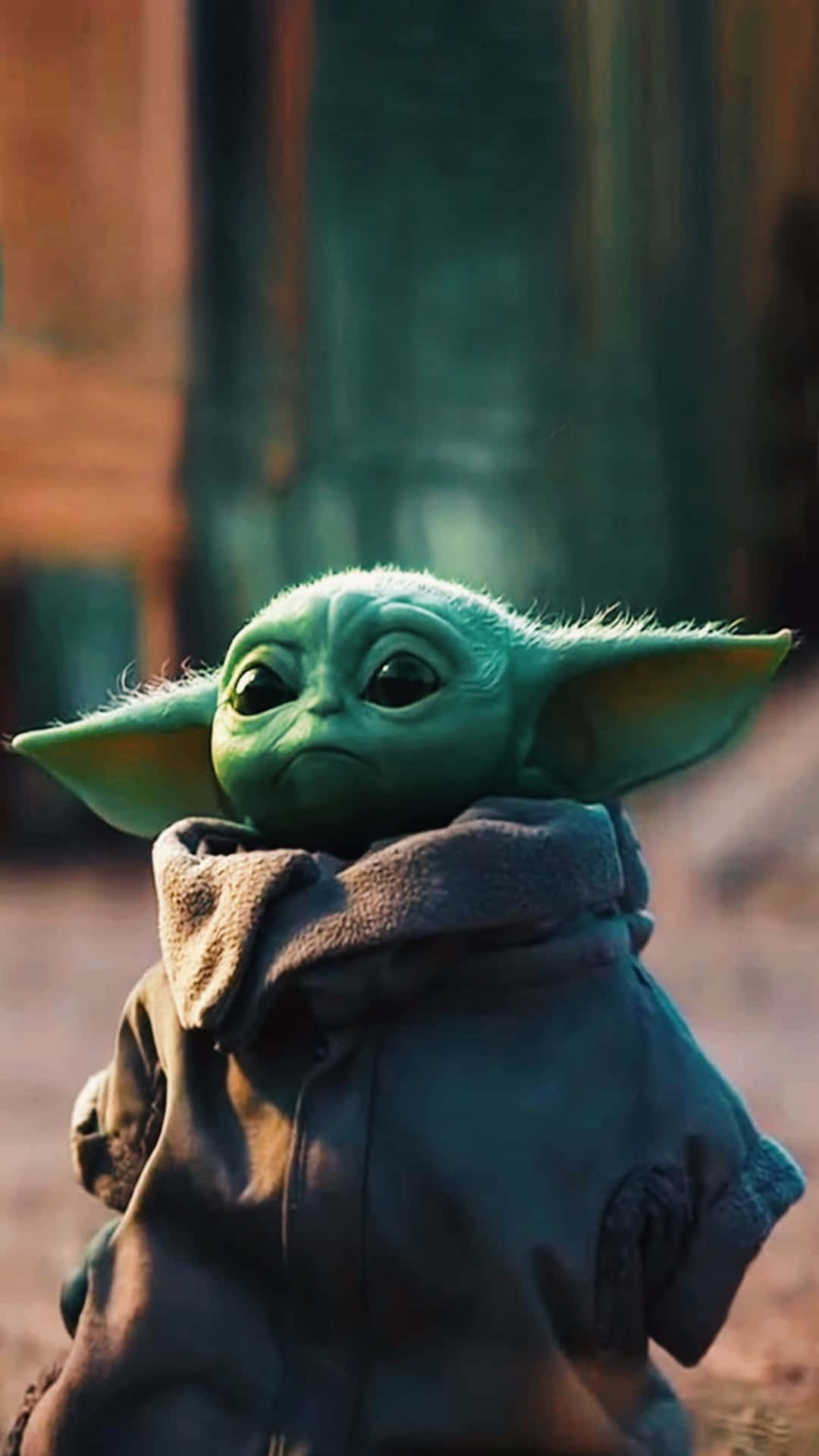 Baby Yoda Phone 桌布 壁紙 — Grogu 綠色外星人特寫，大耳朵，身穿深色長袍，背景模糊暖色調。