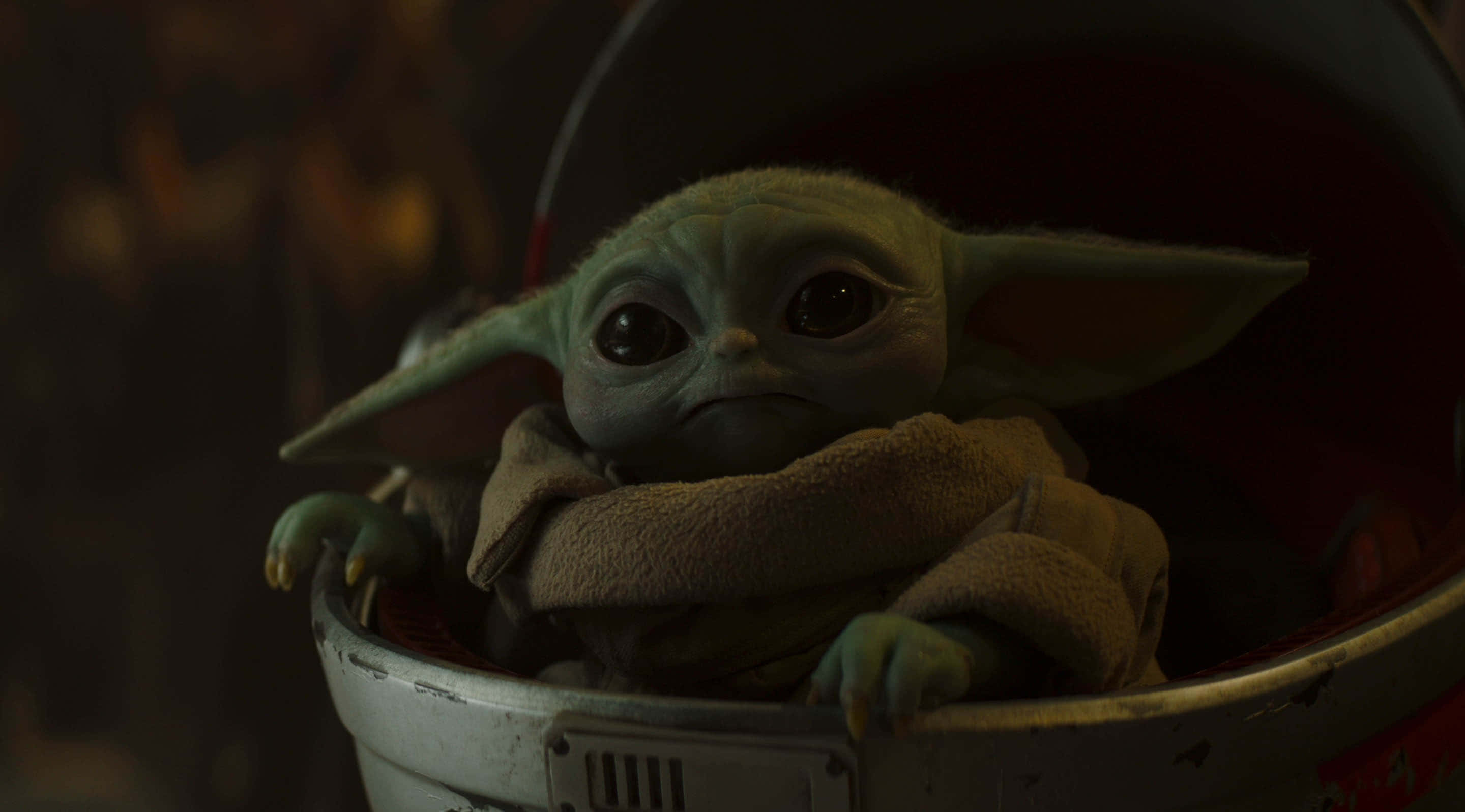 Mandalorian Yoda 桌布 壁紙 — Grogu 蜷縮在磨損的金屬載體中的特寫，柔和的光線突出他大大的耳朵和好奇的眼睛。